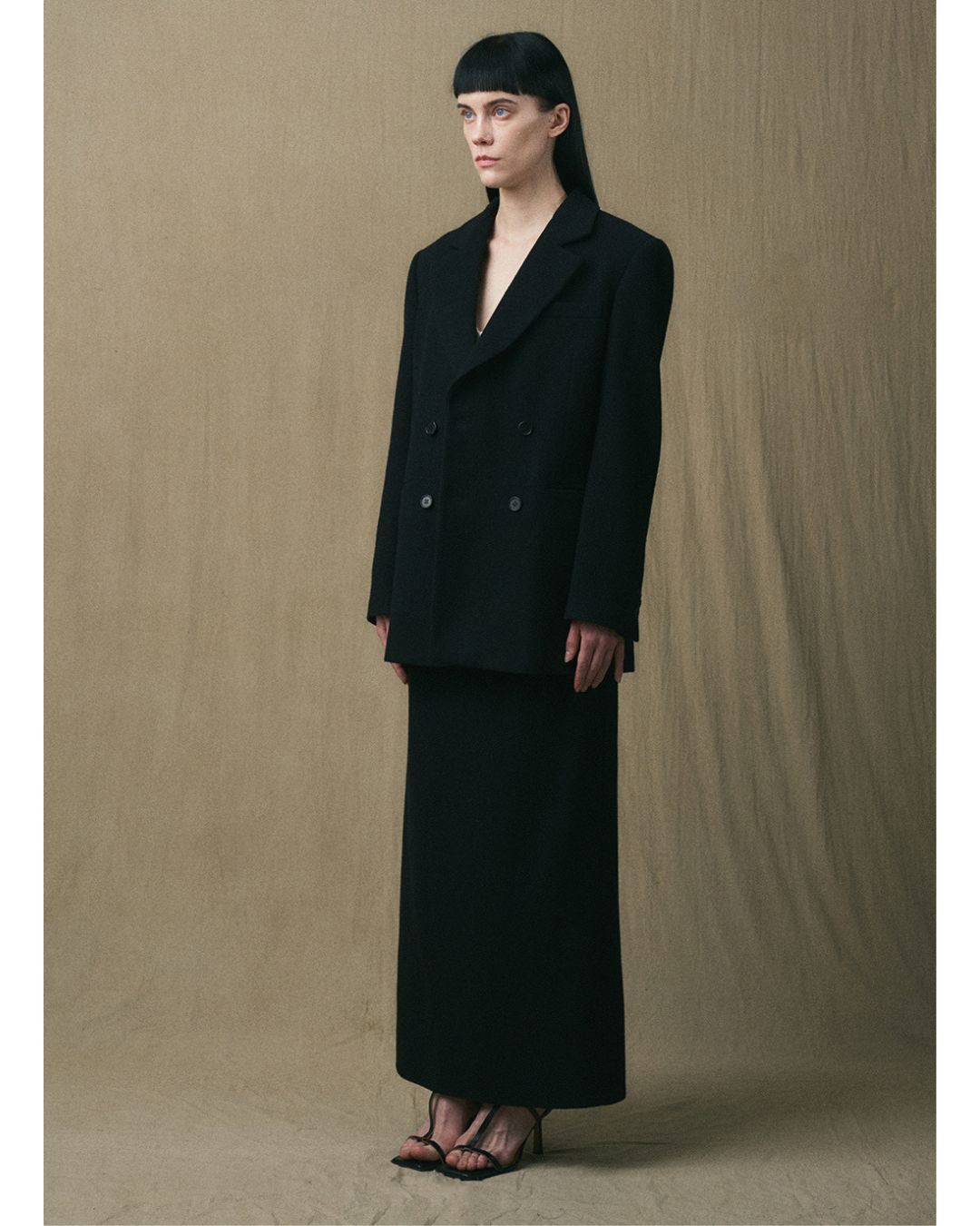 Three-quarter view of the JINSUN black wool jacket styled with the matching maxi skirt