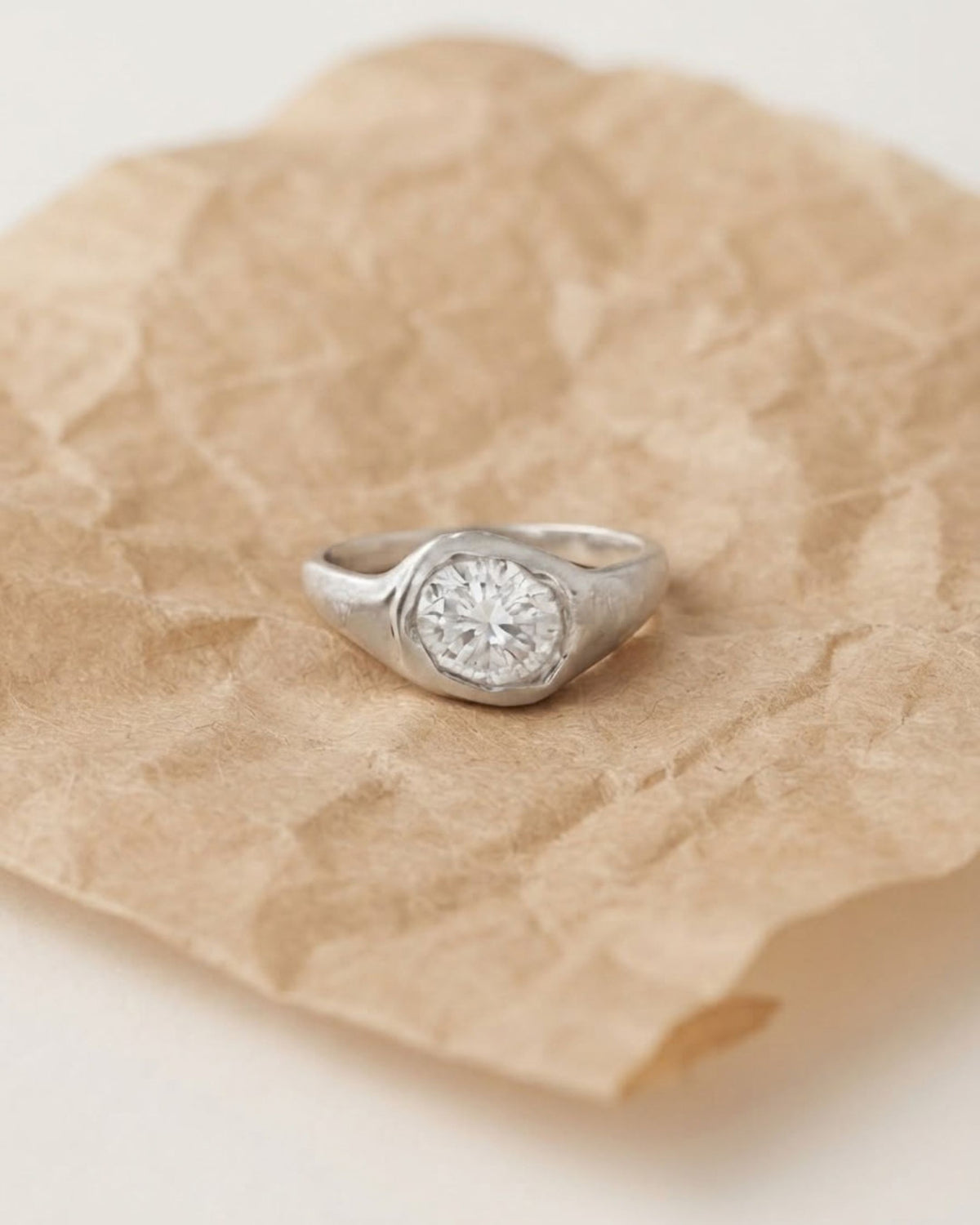 Front view of a sterling silver ring with a round lab-created white stone in a molten organic bezel, on white background