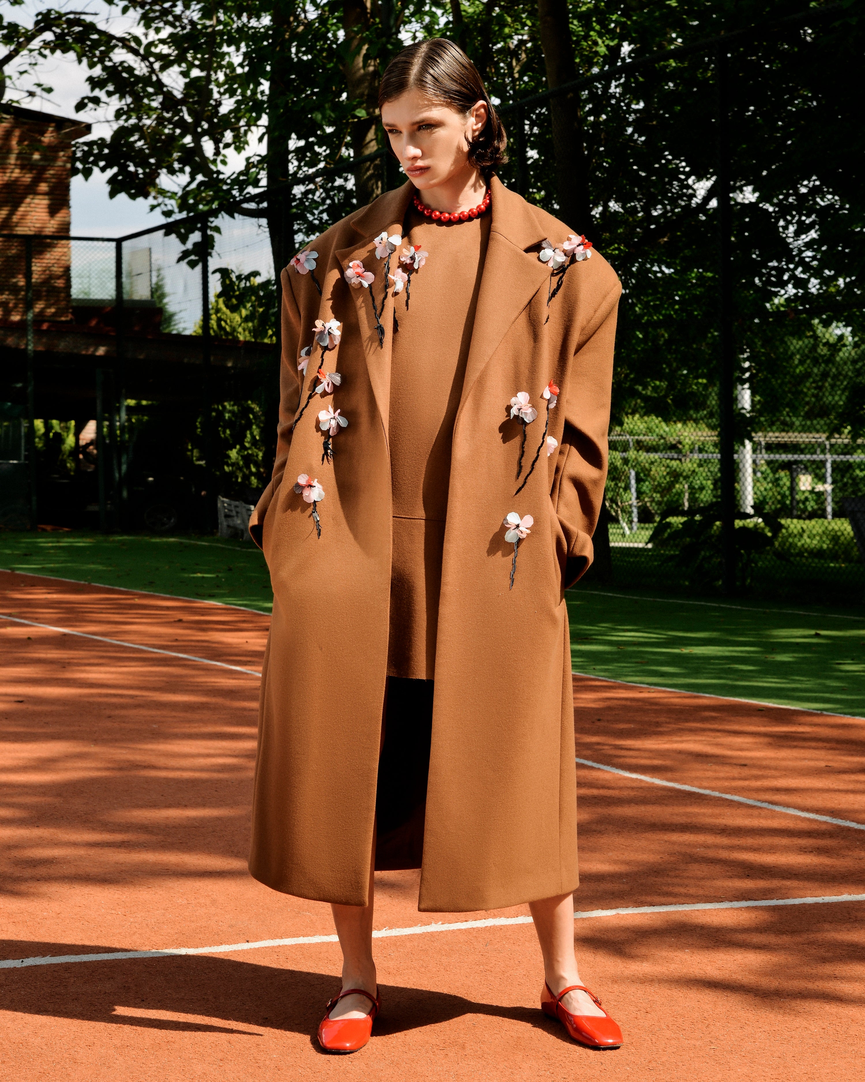 Model wearing the Floris Dress in brown wool with floral embellishments, styled with coordinating outerwear