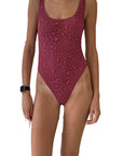 Leslie Amon Condy One Piece in Merlot. A deep rose pink color and textured fabric. A classic one piece swimsuit designer with a high leg and an open scooped back. Shown on model facing front.