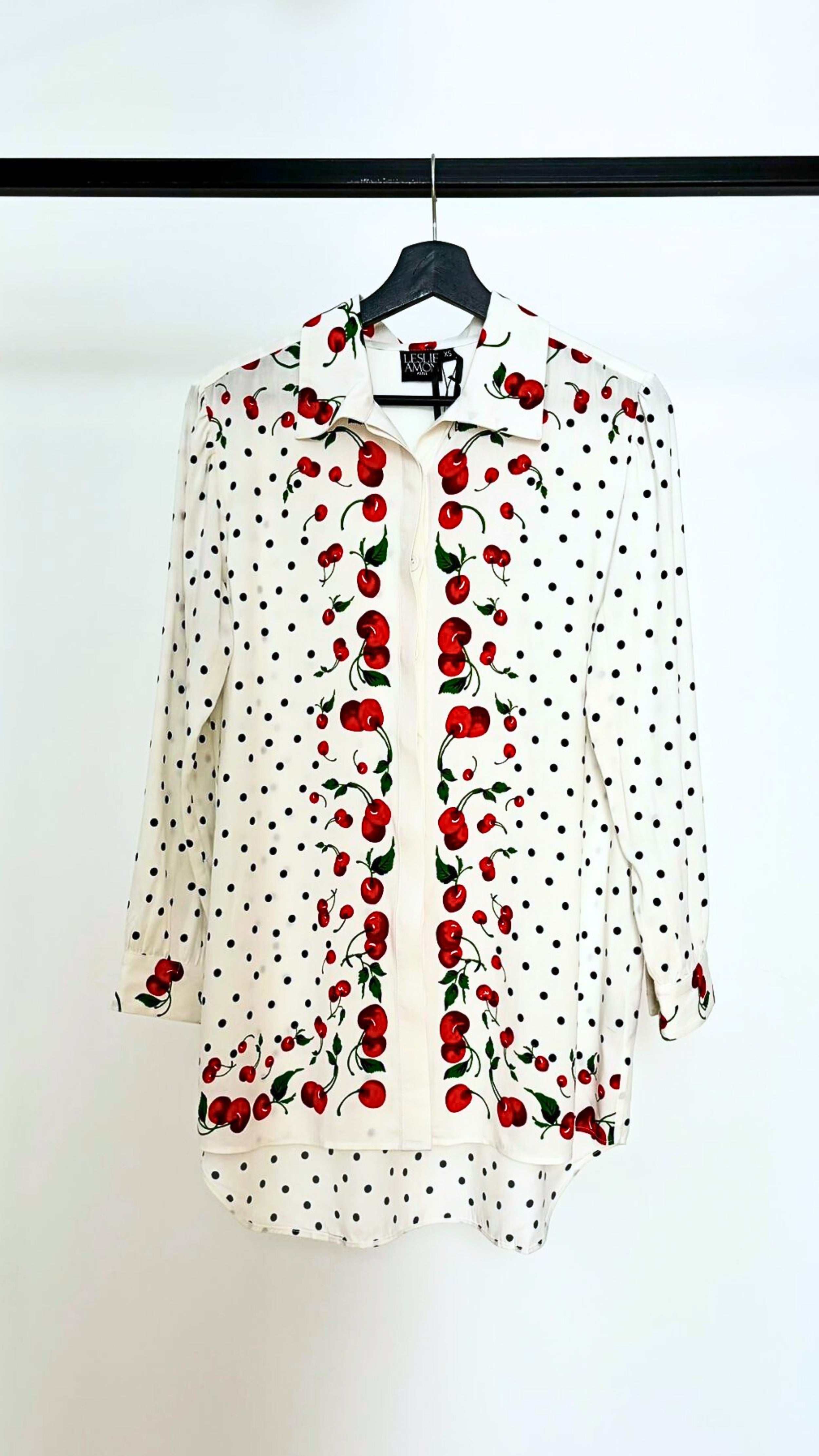 Leslie Amon Oversized Shirt in White Cherry. Oversized blouse in white with red cherry pattern. With button closures up the front, buttoned cuffs and collar. Product photo shown from the front.