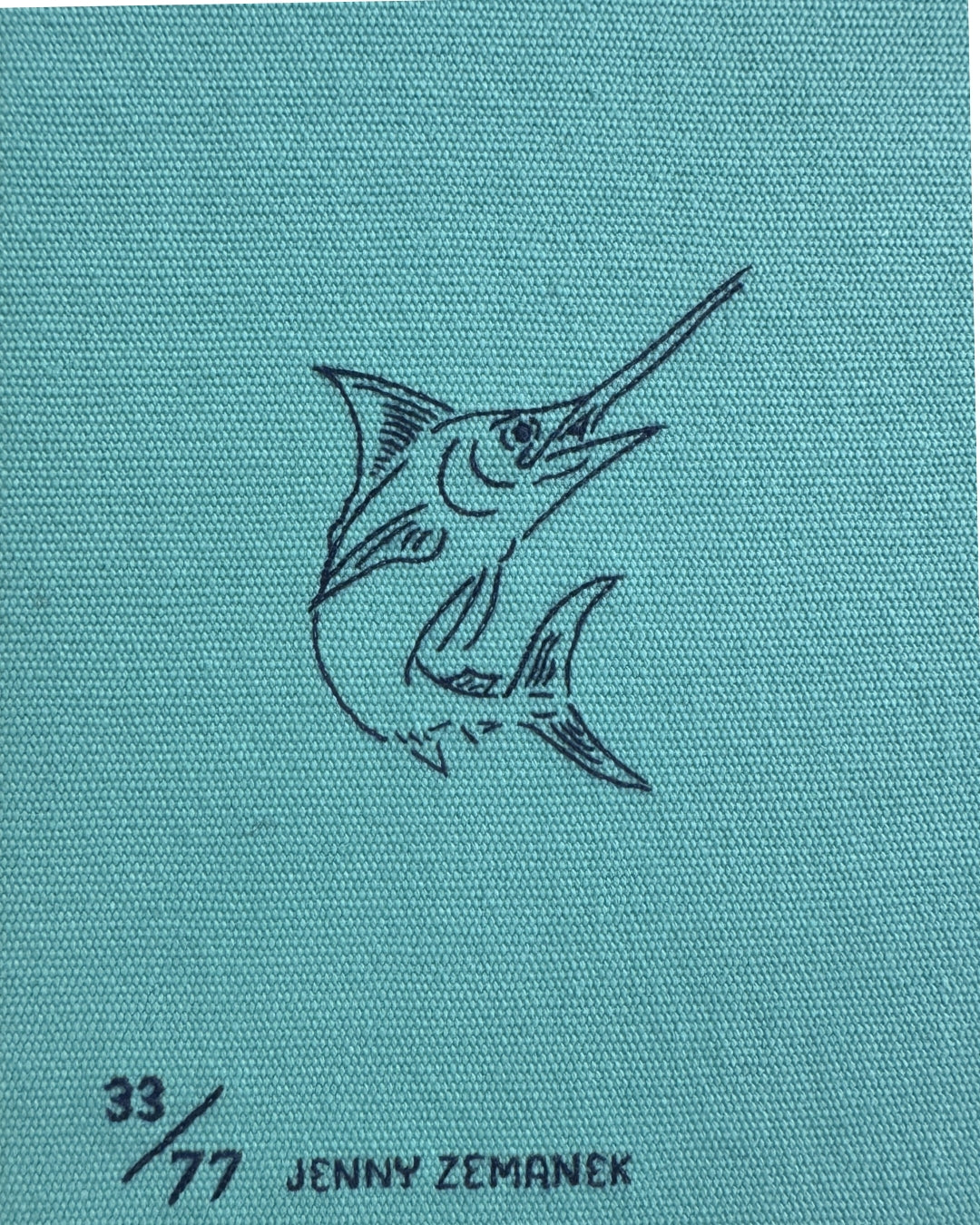 Close-up of the reverse of the Old Man and the Sea clutch showing the embroidered marlin outline in navy on teal cotton, with edition number 33/77 and "Jenny Zemanek" illustrator credit.