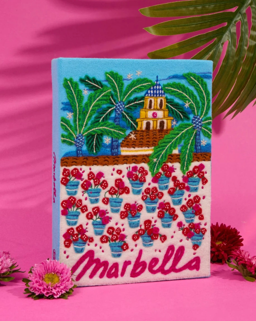 Olympia Le-Tan Marbella book clutch styled against pink background with tropical flowers