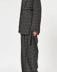 Plan C Checked Black Blazer. Modern suit jacket option in an oversized fit in lightweight wool. Classic black and white check pattern. Shown on model buttoned and belted. Facing to the side.