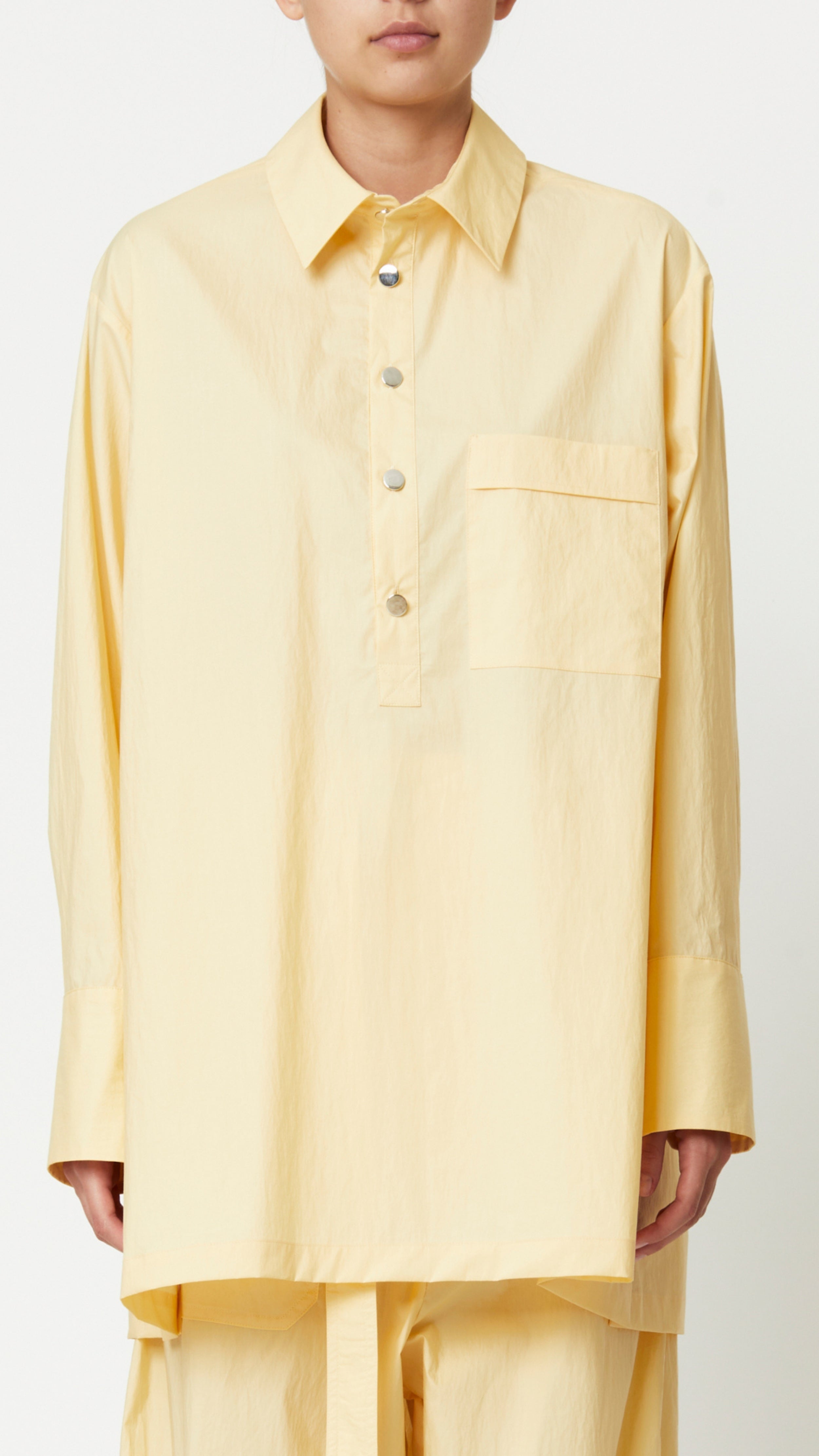 Plan C Eggnog Cotton Shirt A relaxed fit blouse made from light weight cotton in pale yellow and white. With Silver buttons up the front, a chest welt pocket, and a split elongated hem.  Shown on model facing front.
