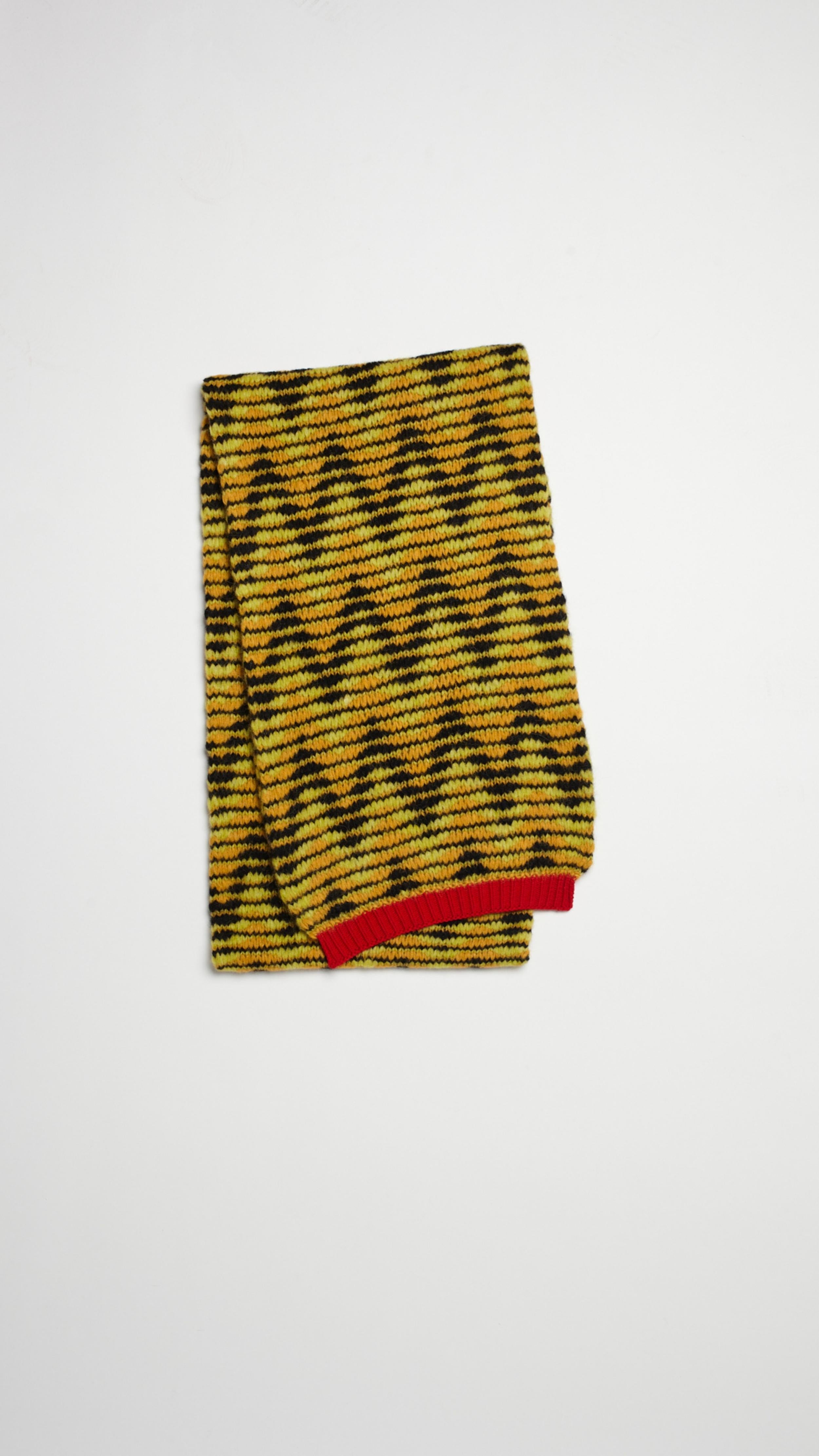 Plan C Jacquard Knit Oversize Scarf in pistachio, black and ochre colored chevron V pattern. Pop of red at the trim. Super oversized made from soft alpaca and wool blend. Photo shown folded. 