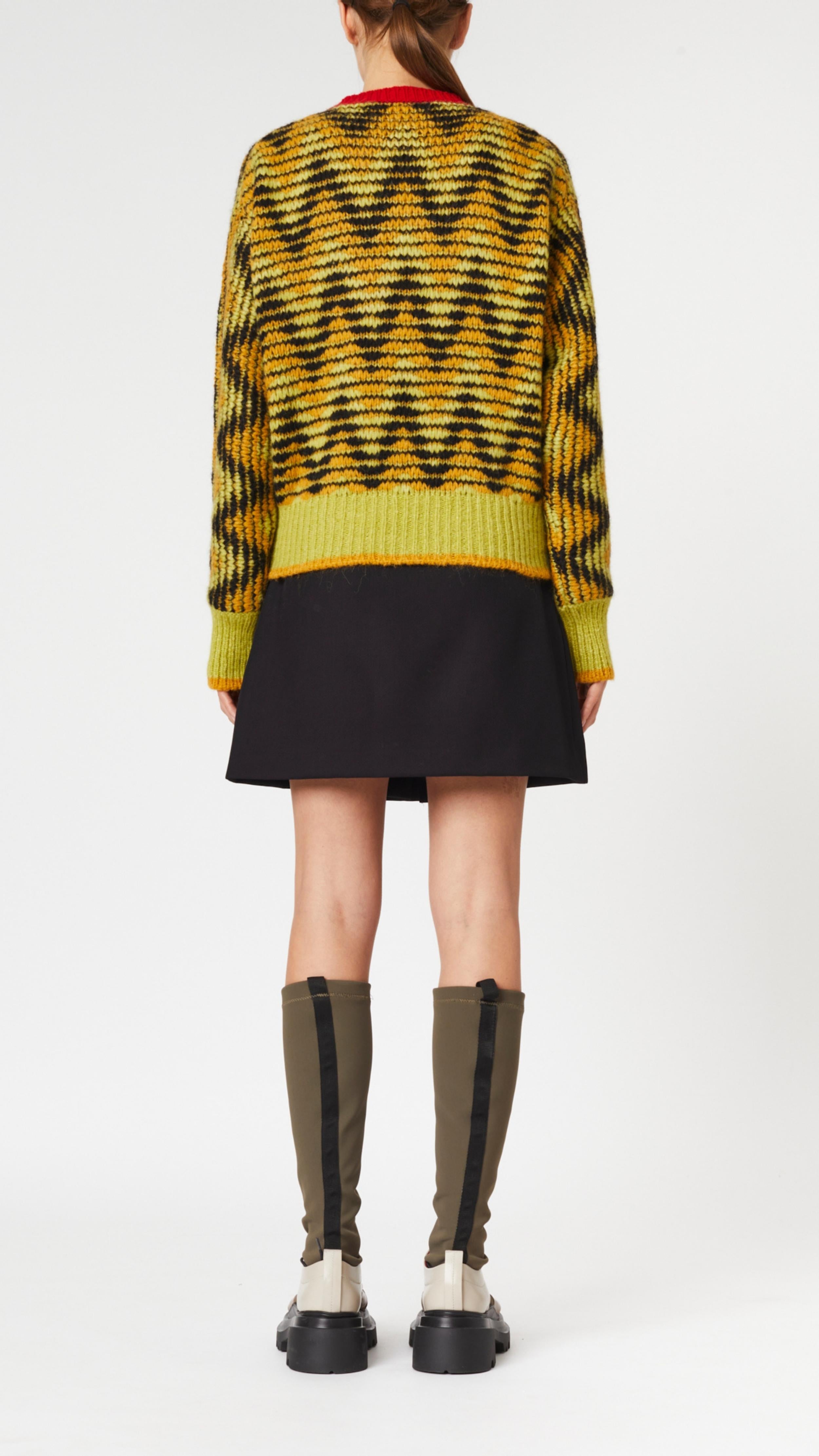 Plan C Long Sleeve Jacquard Knit Sweater.Ppistachio, black and ochre colors in a V chevron print. Red pop of color at the collar. Photo shown on model facing to the back..