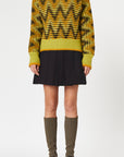 Plan C Long Sleeve Jacquard Knit Sweater.Ppistachio, black and ochre colors in a V chevron print. Red pop of color at the collar. Photo shown on model facing front.