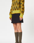 Plan C Long Sleeve Jacquard Knit Sweater.Ppistachio, black and ochre colors in a V chevron print. Red pop of color at the collar. Photo shown on model facing to the side.
