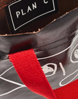Plan C Pili and Bianca Black Mini Shopper. Coated canvas mini shopper style bag with whimsical drawings on either side. Completed with a red handle strap and a long black strap. Close up of interior.