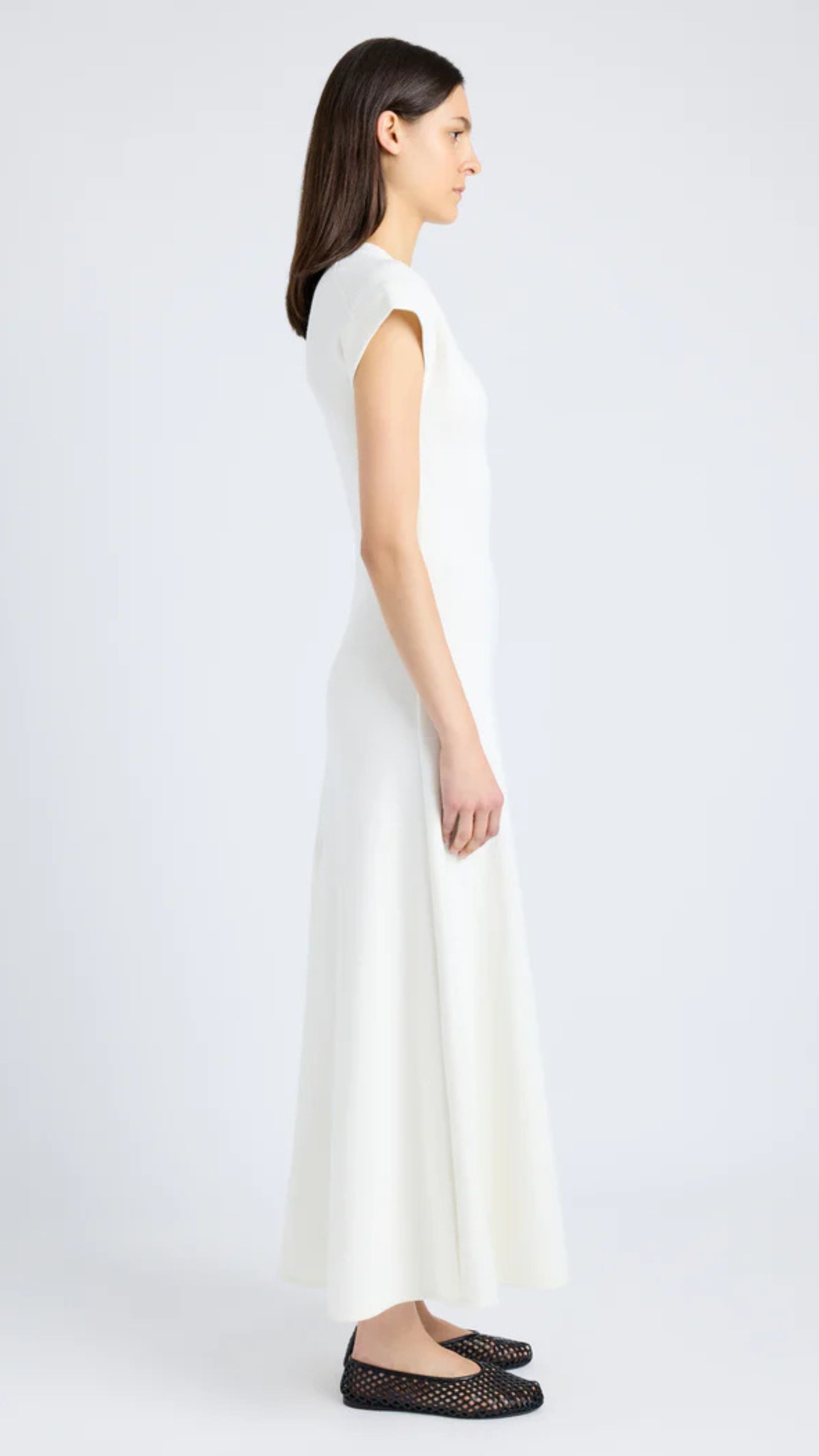 Woman wearing Melanie Dress in white souffle rib with cap sleeves and crew neckline, featuring long A-line skirt, side view.