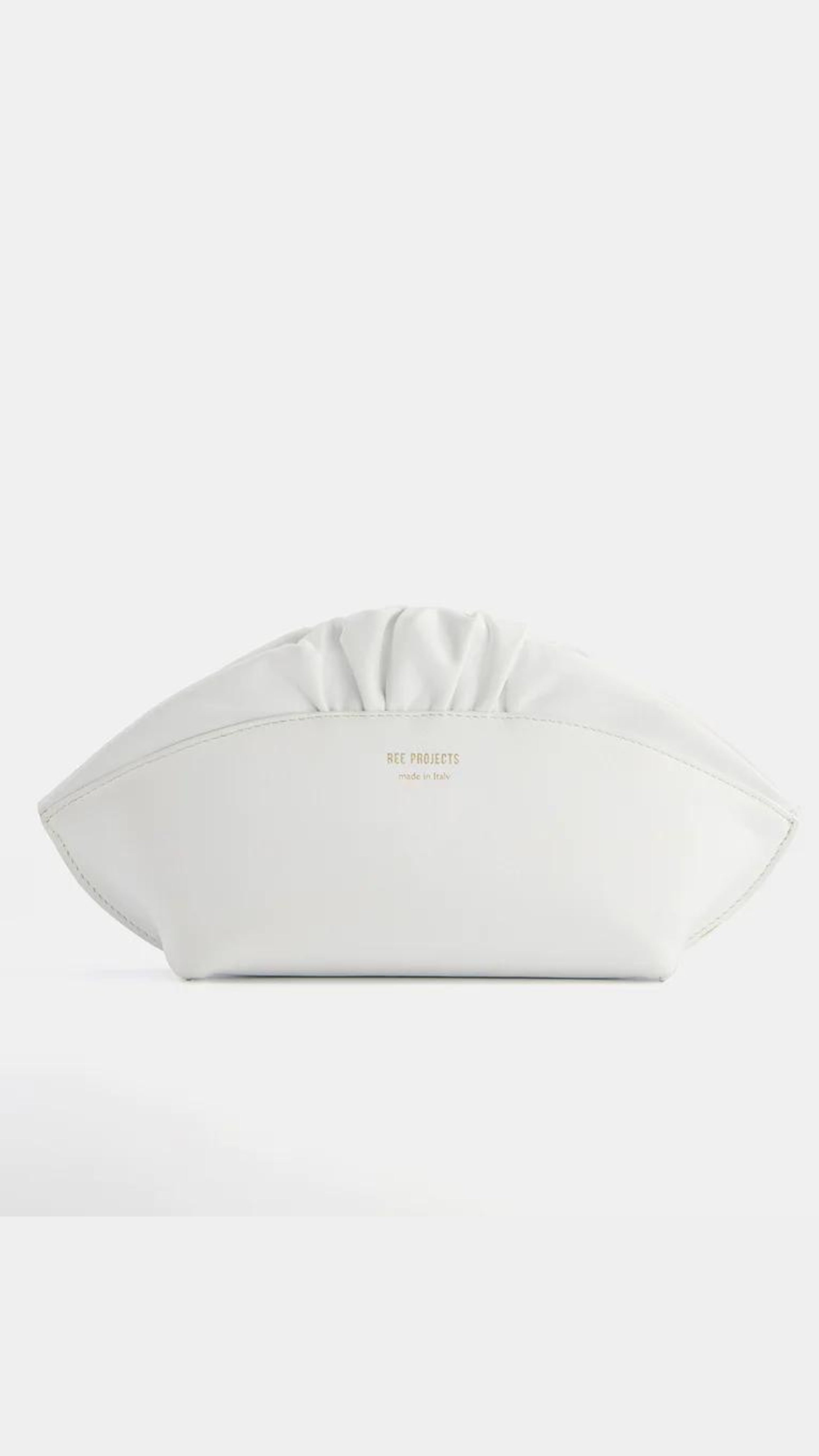 Ree Projects, Ann Baguettina in White. Made in the softest Italian leather this clutch style is perfect for any occasion. It has a slim curved top that is finished with a delicate ruffle and gold hardware. It features a strong magnetic closure and has internal straps to allow it to convert to a shoulder or crossbody bag.  Shown from the front in clutch bag style.