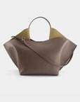 Ree Projects, Ann Tote Bag Medium in Ash Brown.  An understated elegant every day bag in a medium size. Crafted from the softest Italian calf leather, this soft brown grey color purse features the signature folded 'Ree Projects top-line gussets' and a sculptural silhouette. This purse can be used with the top handle or as a crossbody. It features interior pockets and a magnet snap closure. Shown from the back with cross body strap.