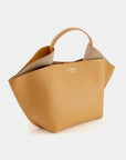 Ree Projects, Anne Tote Mini in Apricot.  An understated elegant every day bag. Crafted from the softest Italian calf leather, this apricot orange  purse features the signature folded 'Ree Projects top-line gussets' and a sculptural silhouette. Its mini-sized size easily fits your phone, tablet and other items. This purse can be used with the top handle or as a crossbody. It features interior pockets and a magnet snap closure.  Shown from a angle