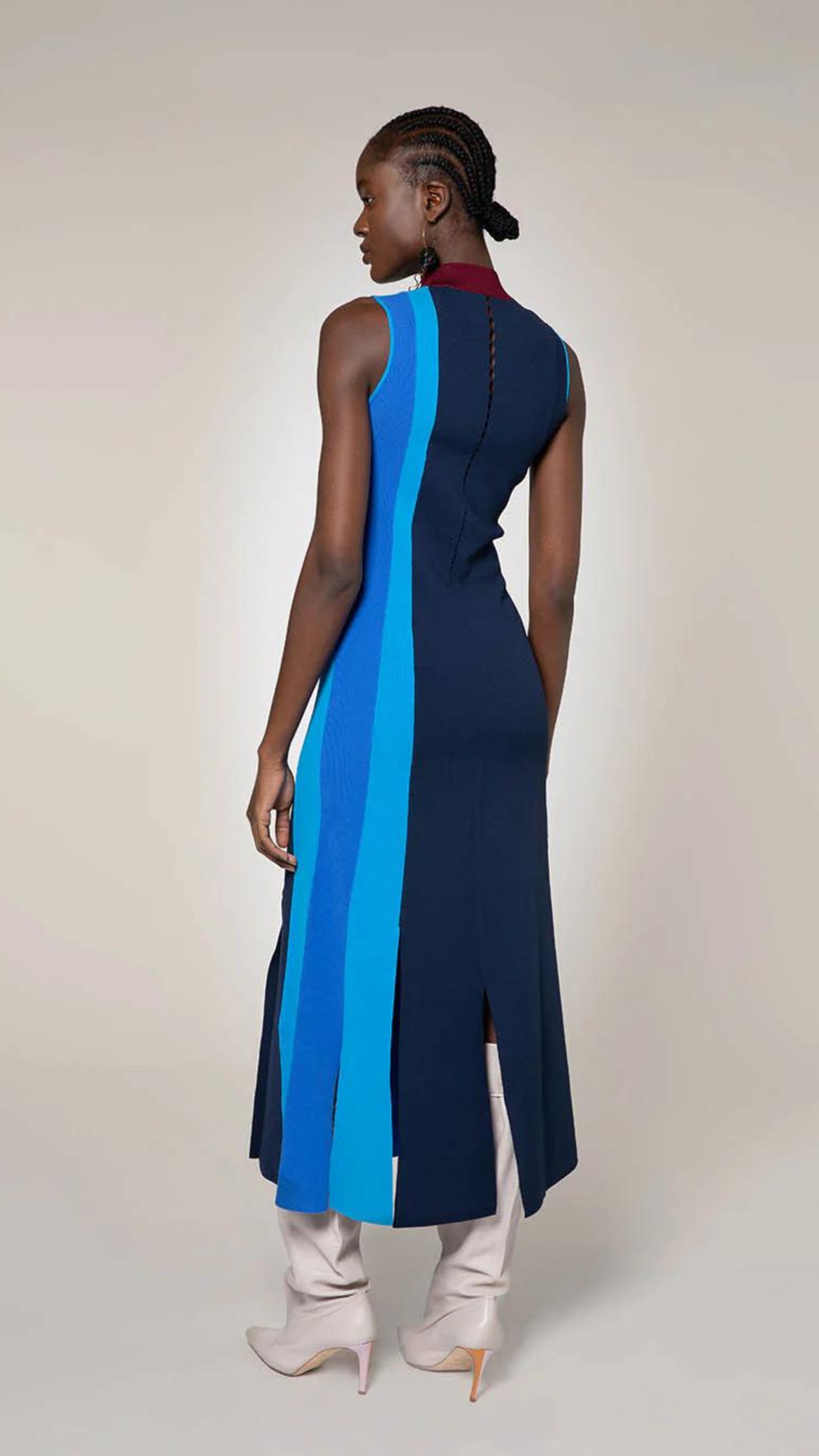Roksanda Matthiola Knit Dress. Lightweight knit dress in varying blue tone vertical panels. With wide fringe bottom it falls to a midi dress length. A contrasting burgundy color. Shown on model facing back.