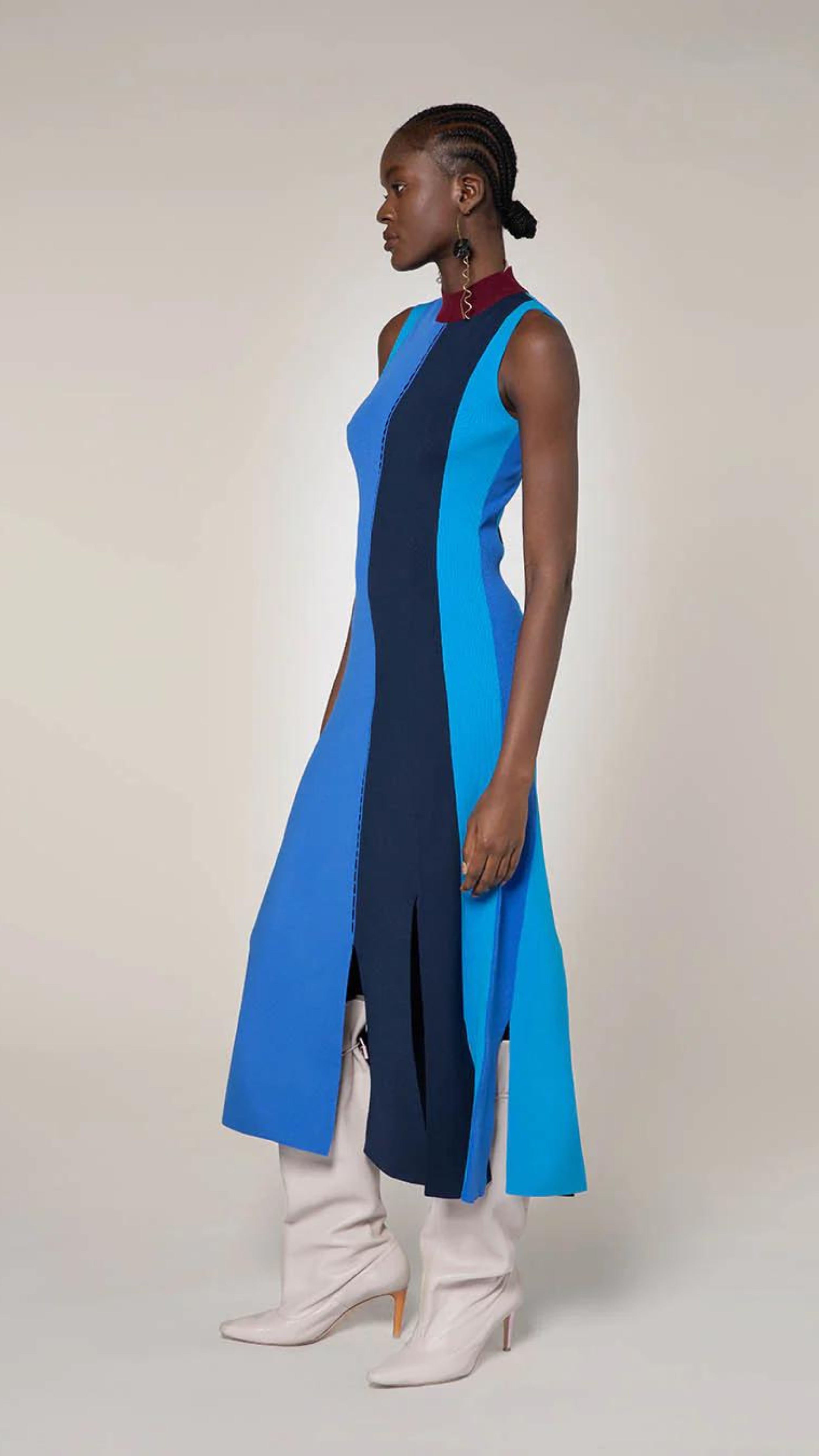Roksanda Matthiola Knit Dress. Lightweight knit dress in varying blue tone vertical panels. With wide fringe bottom it falls to a midi dress length. A contrasting burgundy color. Shown on model facing side.