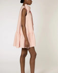 Roksanda Rosalina Dress. Soft pink with fun oversize twisted bow at neckline. Mini dress length with a dropped waist and pleated skirt panel. Shown on model facing back.