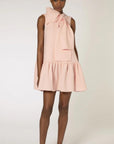 Roksanda Rosalina Dress. Soft pink with fun oversize twisted bow at neckline. Mini dress length with a dropped waist and pleated skirt panel. Shown on model facing front.
