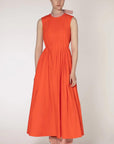 Roksanda The Prinesa Dress. Classic elegant orange cotton dress with a rounded neckline, fitted waist and pleated midi length skirt. Highlighted with a pale pink ribbon collar that ties at the nape of the neck. Shown on model facing front.