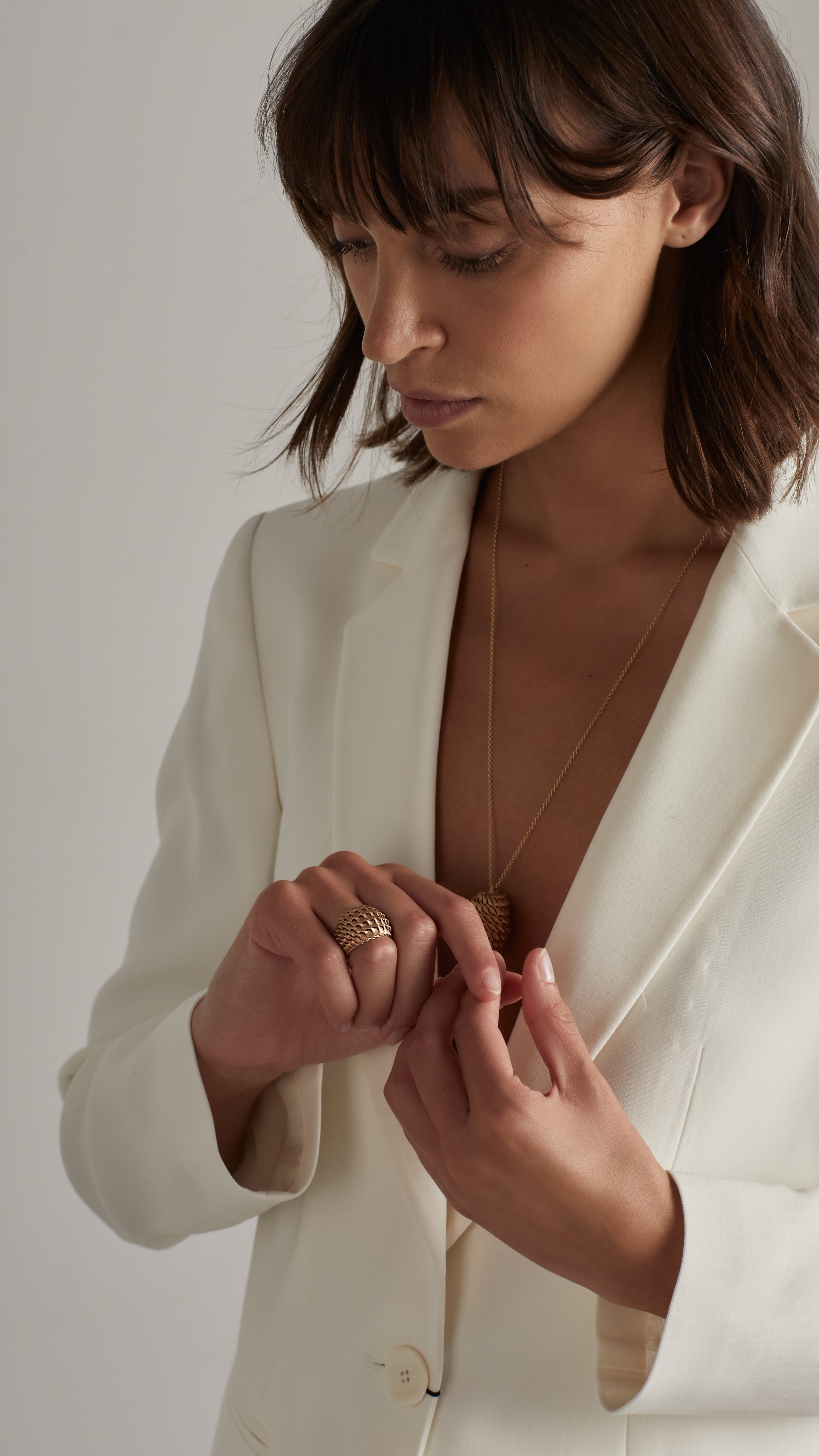 Woman wearing white blazer, showcasing a gold Emi Cocktail Ring with architectural design and fine jewelry detailing.