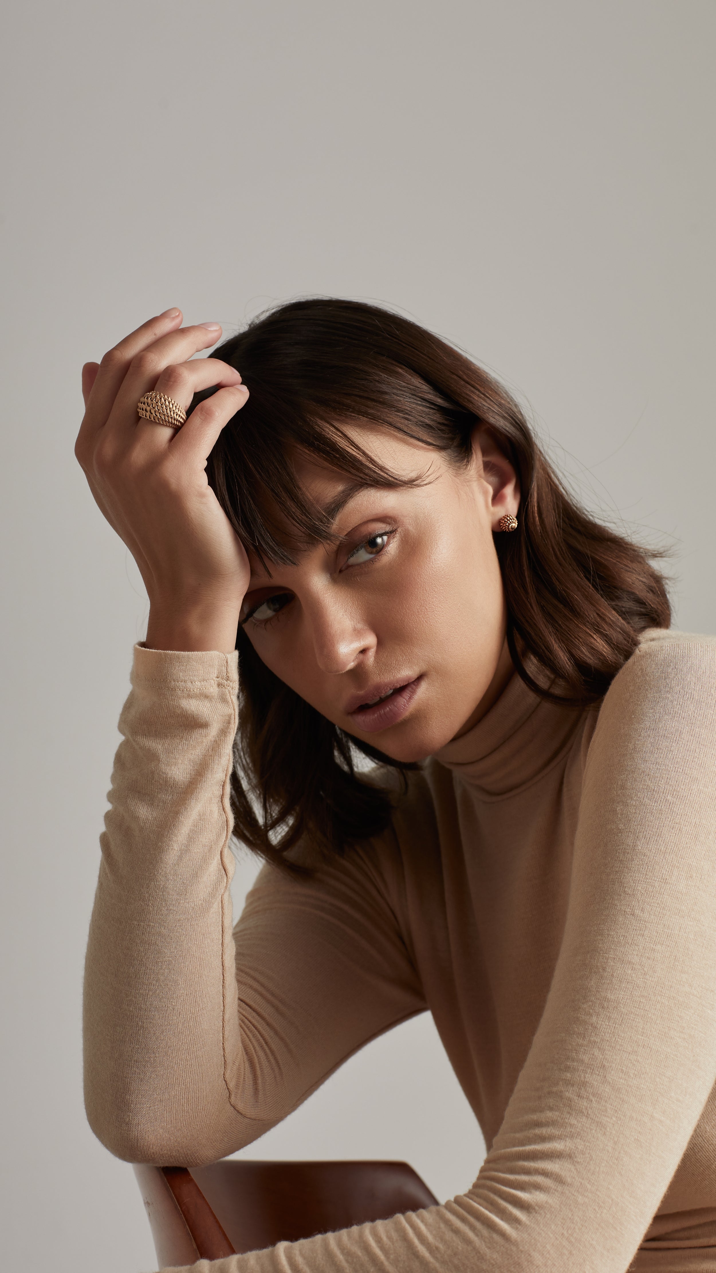 Woman wearing Emi Cocktail Ring, showcasing elegant 18K gold design with architectural features, posed thoughtfully.