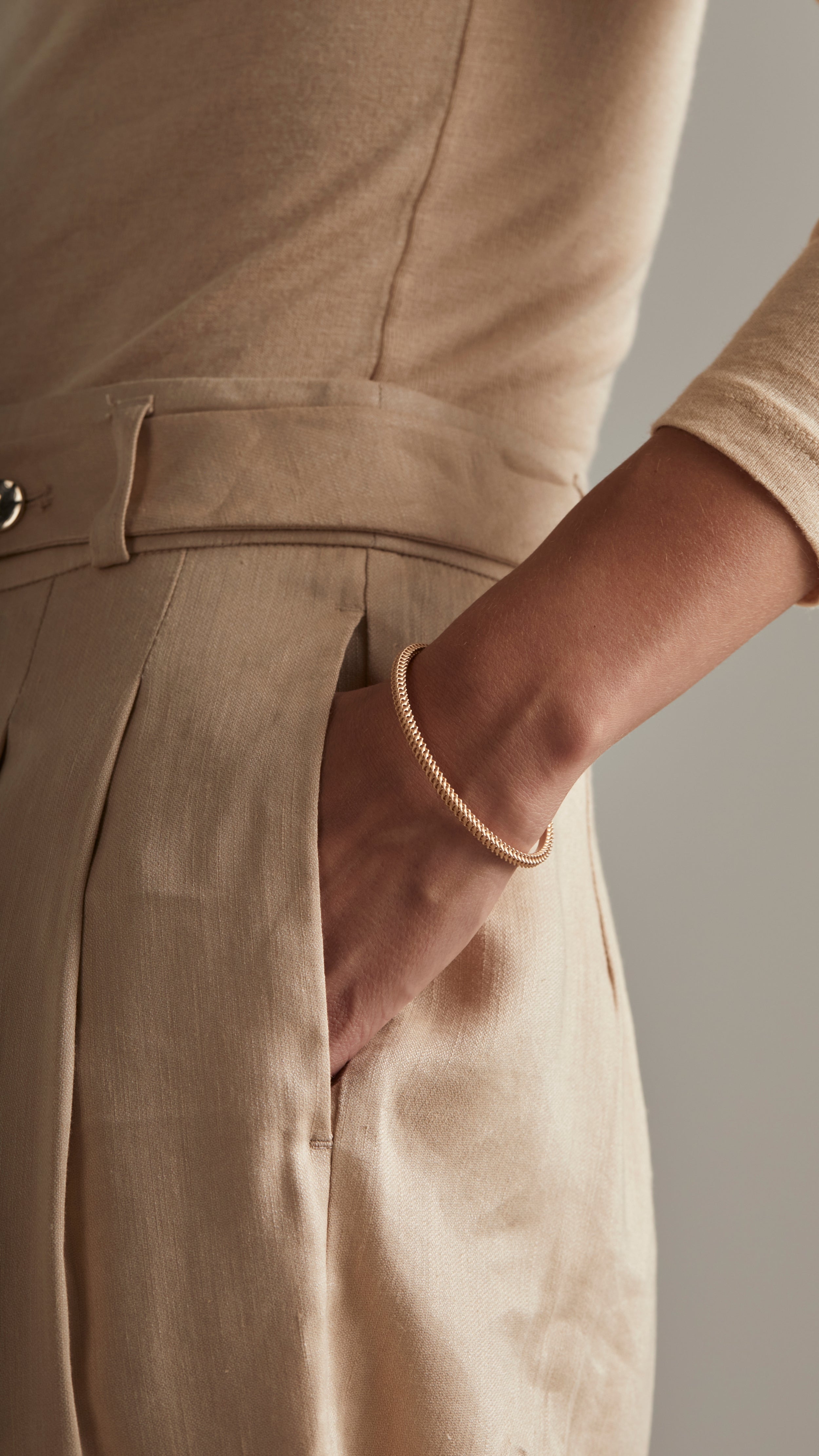 Woman wearing 18K gold Ina Bangle with interwoven grid-like shells and smooth inner surface, paired with beige outfit.