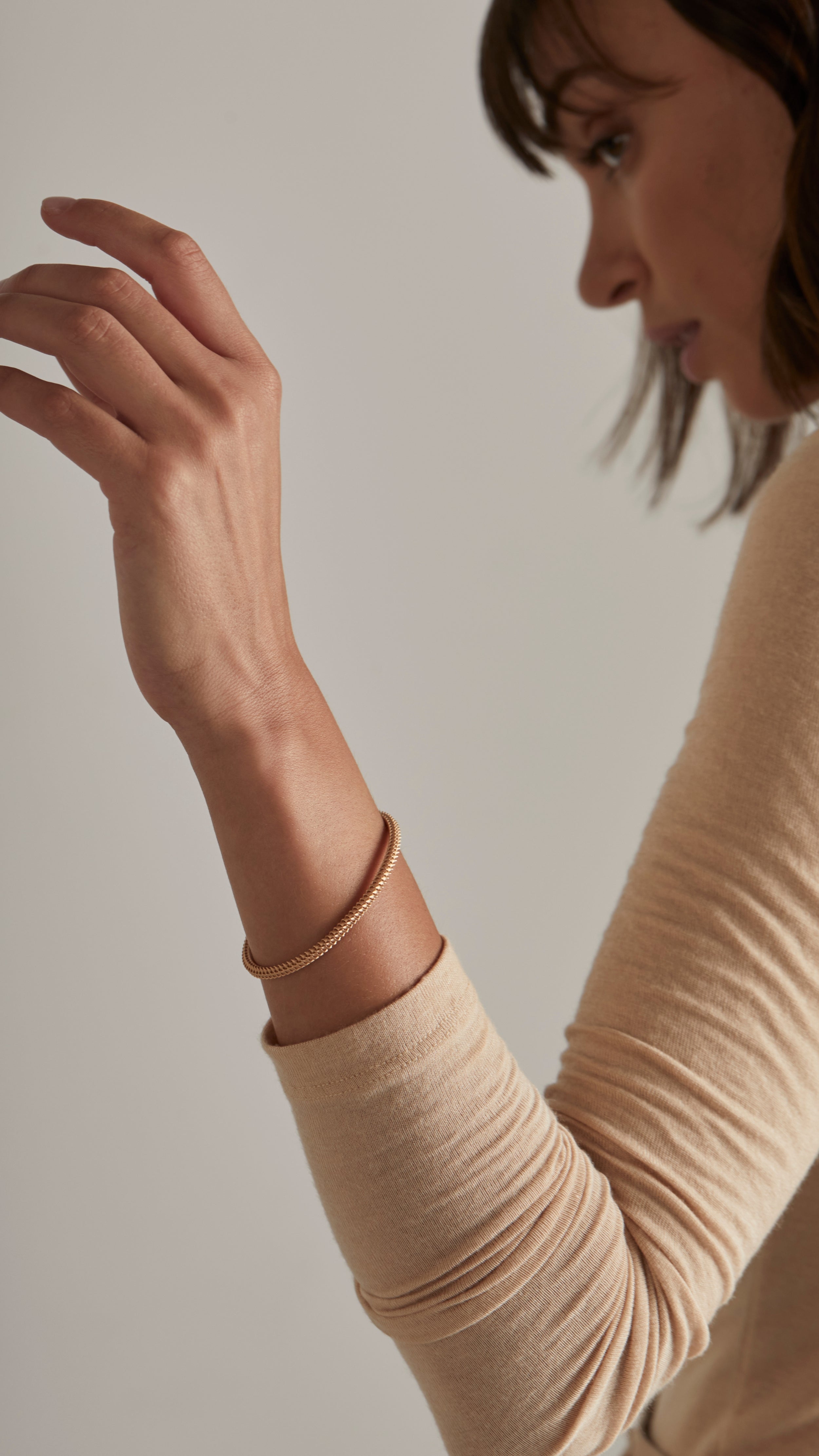 Woman wearing an elegant 18K gold Ina Bangle with interwoven grid-like shells and smooth inner surface, showcasing modern architectural design.