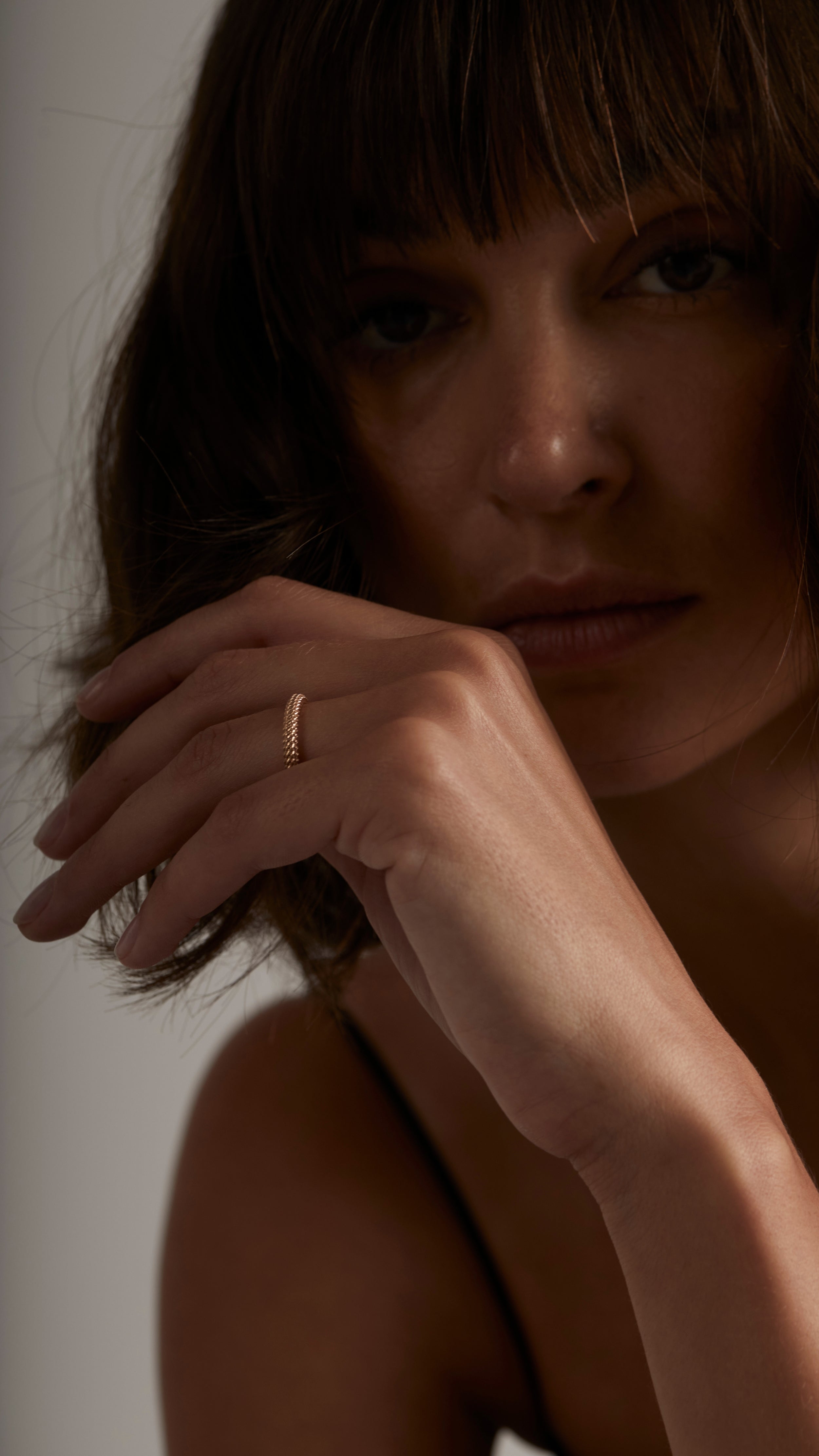 Woman wearing Nio Ring, a 18K gold fine jewelry piece with a thin eternity band of interwoven strands, showcasing elegance and modern design.