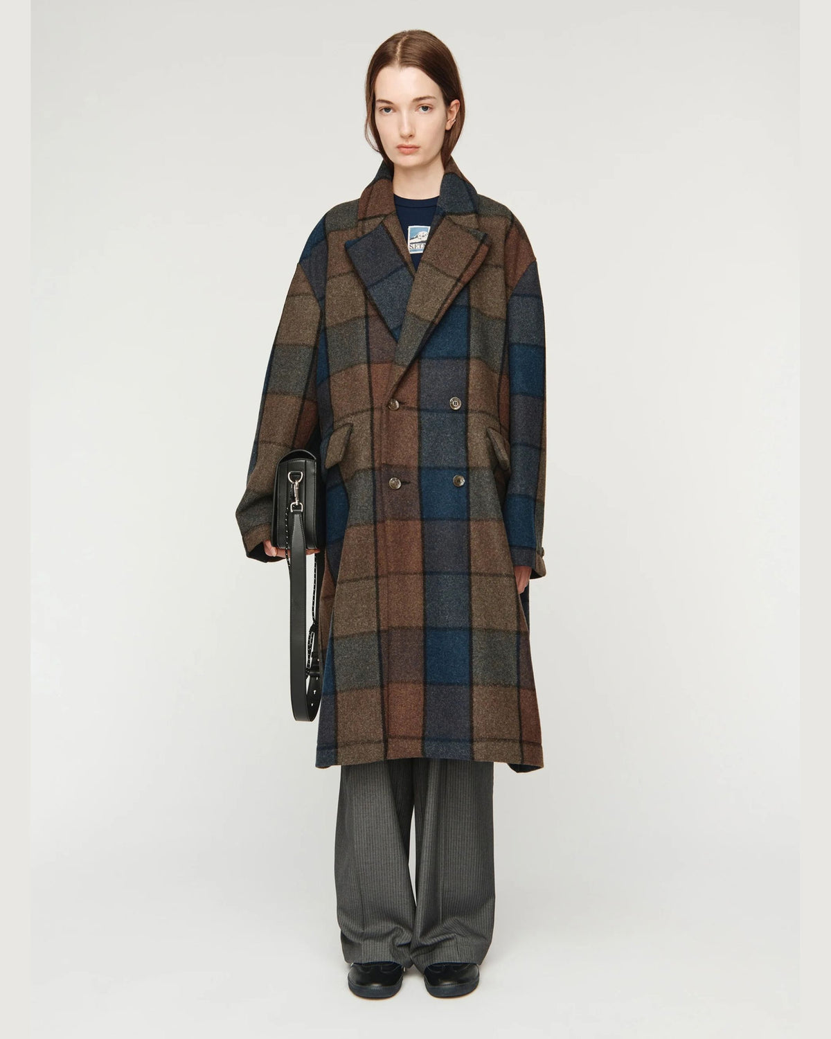 Song for the Mute Double Breasted Overcoat in Bear Check, front view on model holding bag