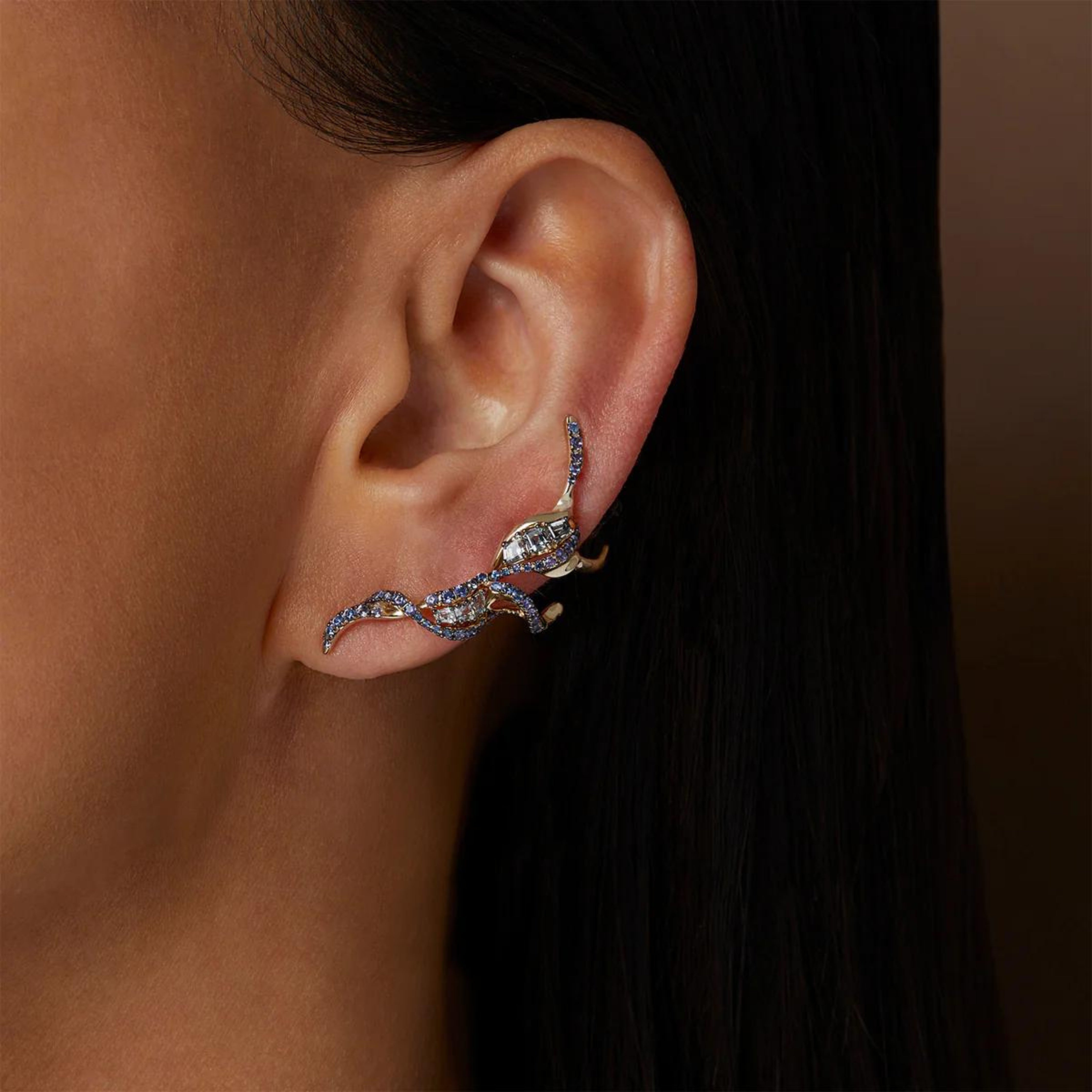 Bibi van der Velden Puff Ear Climber in Blue Sapphire. shades of blue and grey sapphires and spinels adorn the Puff Ear Climber&#39;s 18k white gold tendrils. Delicately crafted, this climber elegantly pierces the ear lobe and sweeps up the ear&#39;s outer edge. Photo of model wearing earring.