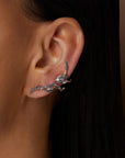 Bibi van der Velden Puff Ear Climber in Blue Sapphire. shades of blue and grey sapphires and spinels adorn the Puff Ear Climber's 18k white gold tendrils. Delicately crafted, this climber elegantly pierces the ear lobe and sweeps up the ear's outer edge. Photo of model wearing earring.
