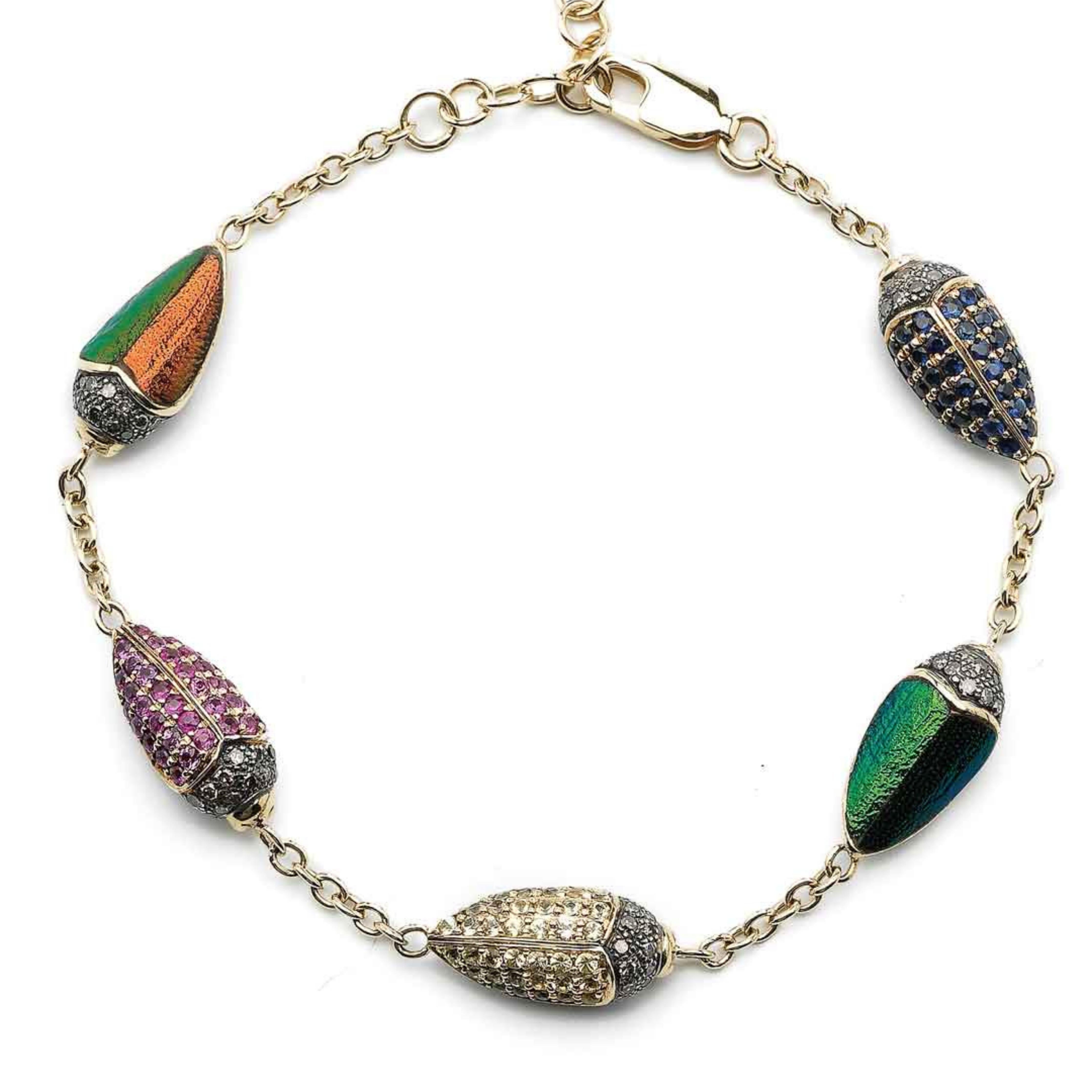 Bibi van der Velden Scarab Multi Color Bracelet. Five scarabs charms connected with 18k yellow gold and sterling silver chains form this charm bracelet.  Each scarabs featured here are set with real scarab wings, brown diamonds, blue sapphires, and tsavorites. Bracelet shown from top view.