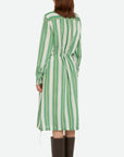 Wales Bonner Balance Dress Made in Italy in a lightweight silk blend. The midi dress has long sleeves, a white collared neck, and green and white stripes. The shirt dress has an adjustable drawstring waist, buttons up the front, and deep front pockets. Shown on model facing the back.