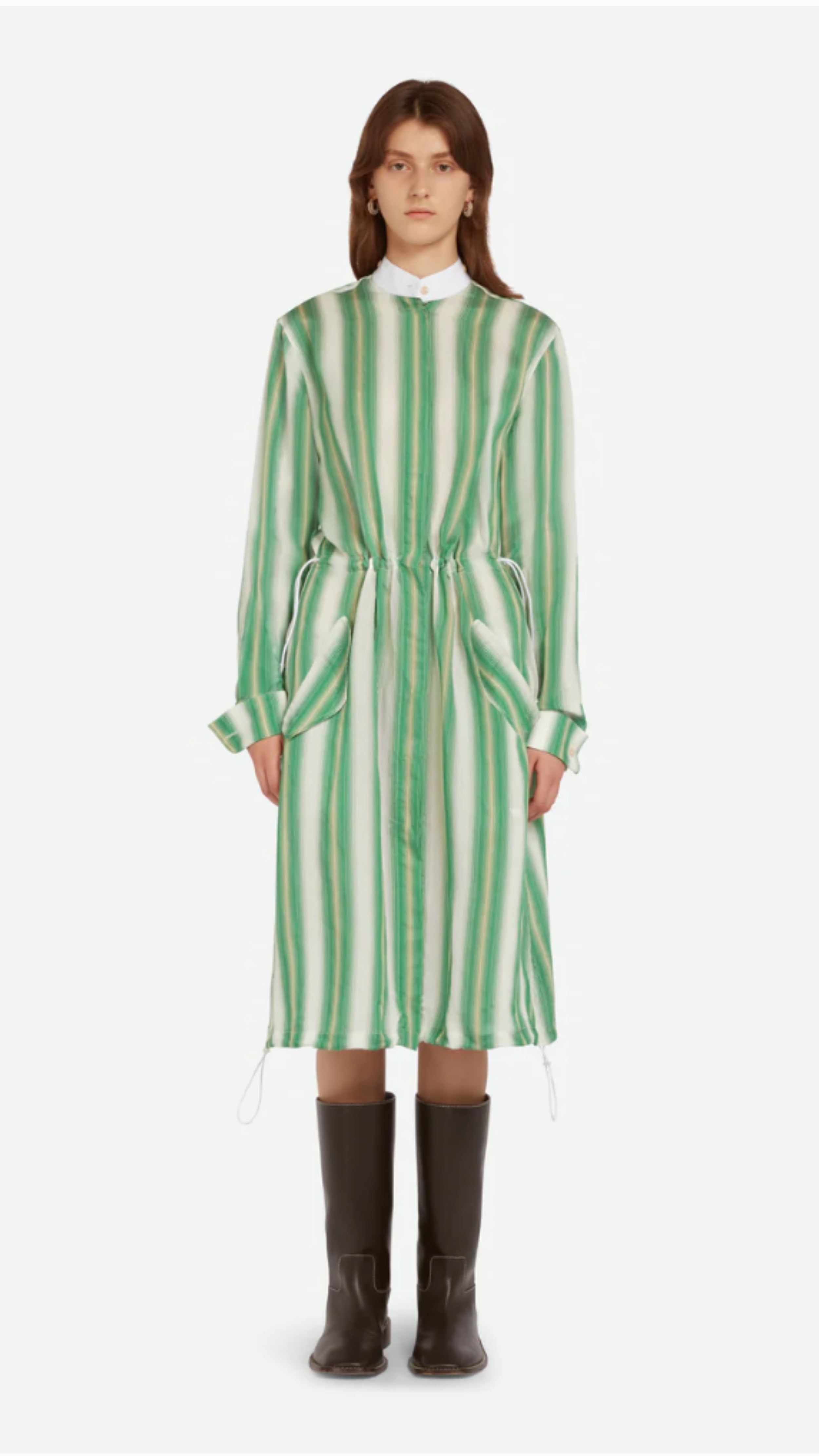 Wales Bonner Balance Dress Made in Italy in a lightweight silk blend. The midi dress has long sleeves, a white collared neck, and green and white stripes. The shirt dress has an adjustable drawstring waist, buttons up the front, and deep front pockets. Shown on model facing front.