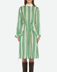Wales Bonner Balance Dress Made in Italy in a lightweight silk blend. The midi dress has long sleeves, a white collared neck, and green and white stripes. The shirt dress has an adjustable drawstring waist, buttons up the front, and deep front pockets. Shown on model facing front.