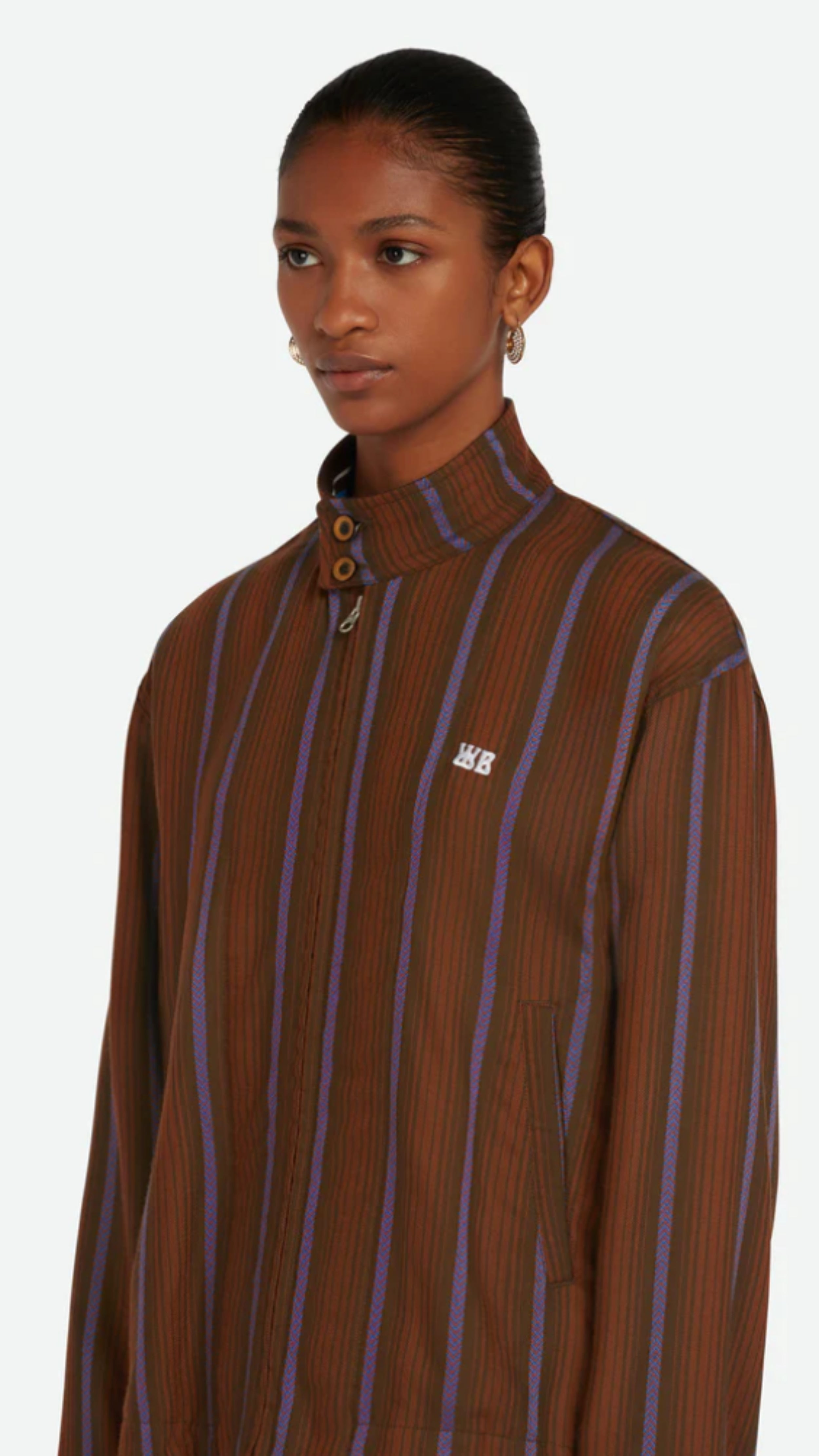 Wales Bonner Life Jacket Italian-made jacket crafted from lightweight herringbone wool in deep brown and blue stripe colors. This coat features long sleeves and a front zipper. Shown on model facing front and close up.