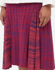 Wales Bonner Nile Skirt This A-line midi skirt features an elastic waist and beautiful pleats at the mid-thigh. Woven striped pattern in red and purples. The skirt falls to knee length. Detail photo of skirt on model.