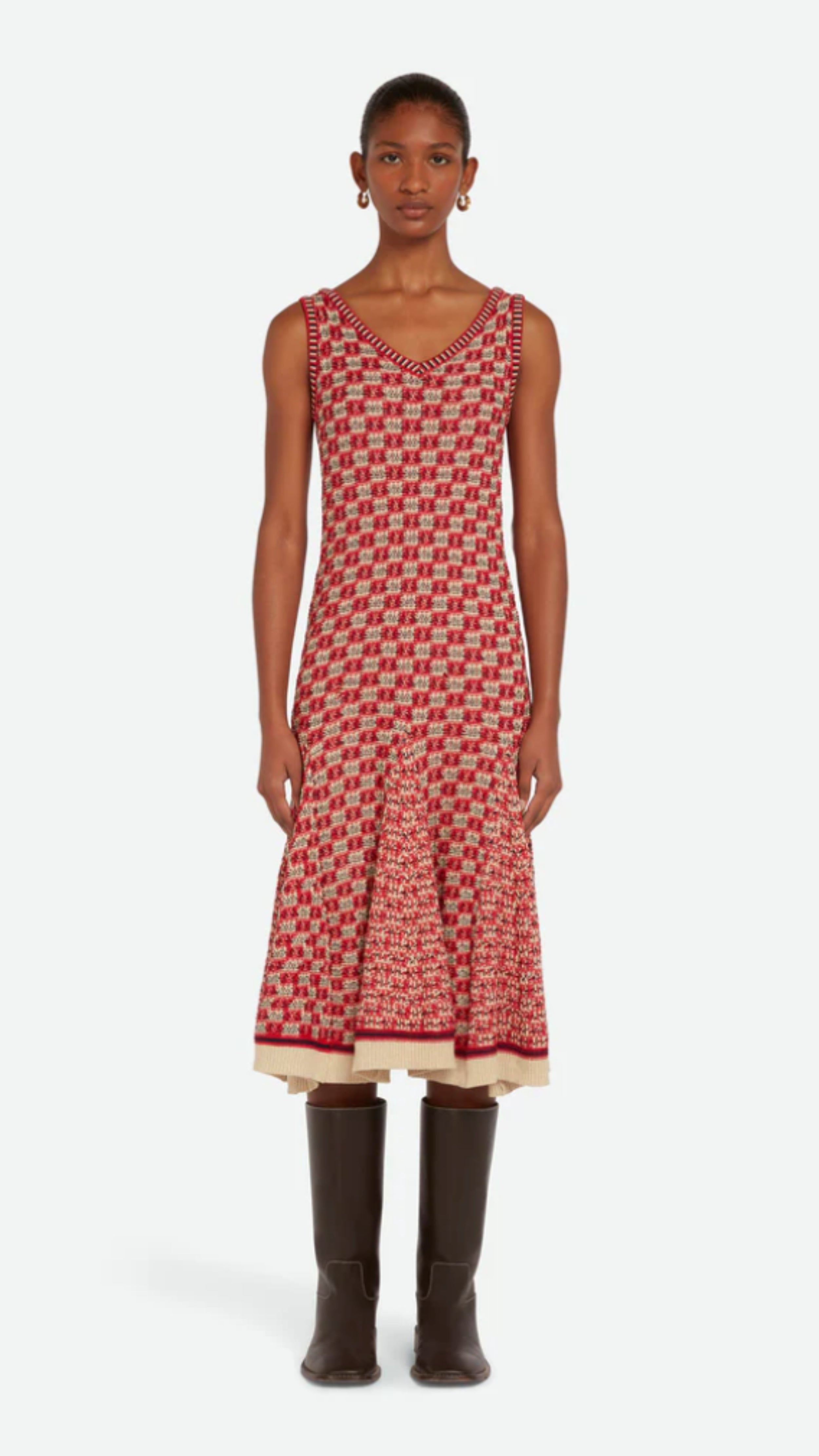 Wales Bonner Soar Godet Dress Woven in an light weight summer Italian cotton knit. This midi length dress has a checkered pattern in red, ivory and black. It has a v-neckline and slightly flared skirt that falls just below the knee. Shown on model facing front.