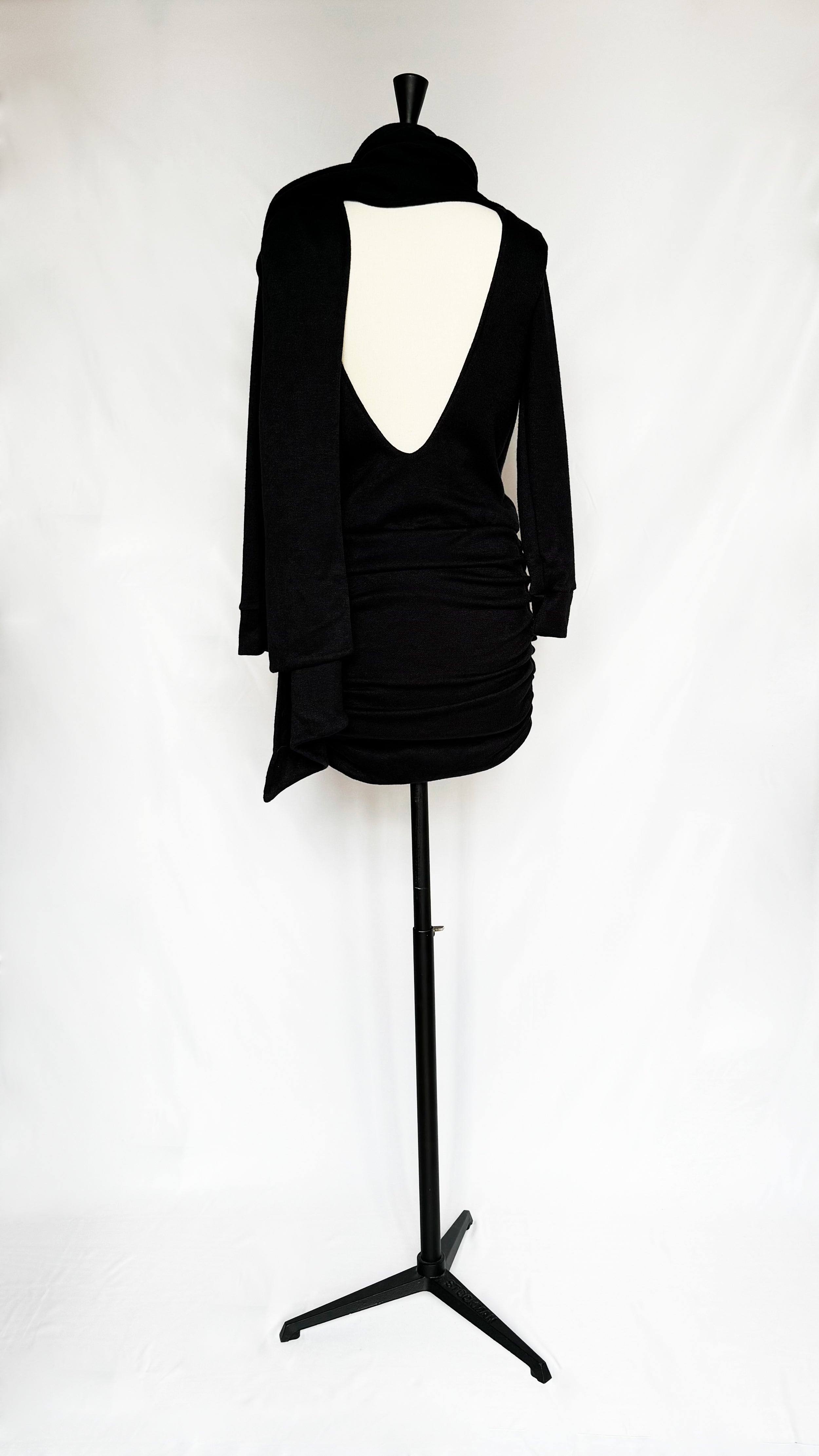 Black Gstaad Mini Dress with open back, long sleeves, built-in scarf, and ruched skirt by Leslie Amon on a mannequin.