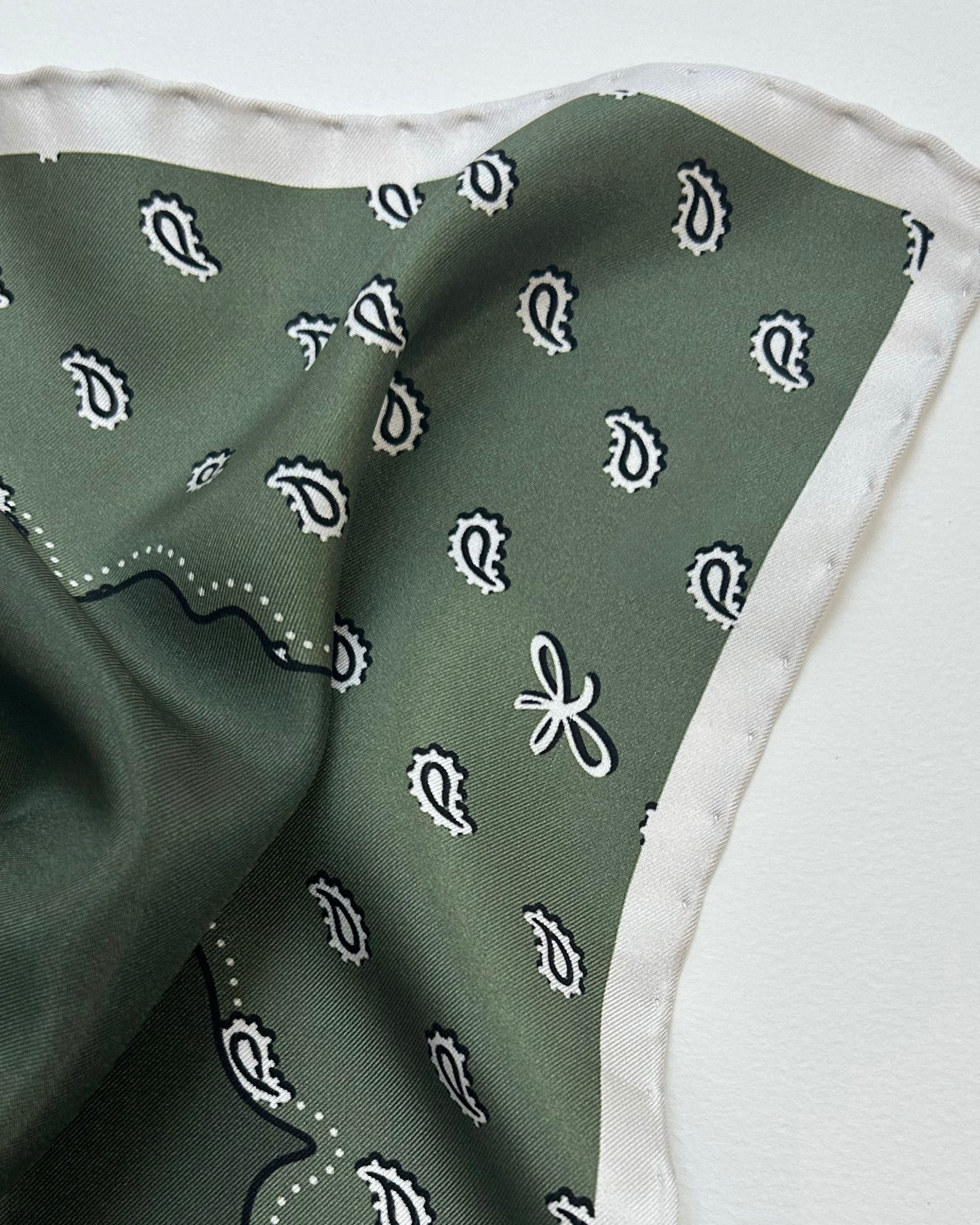 Close-up of olive green silk scarf with paisley motif and white border
