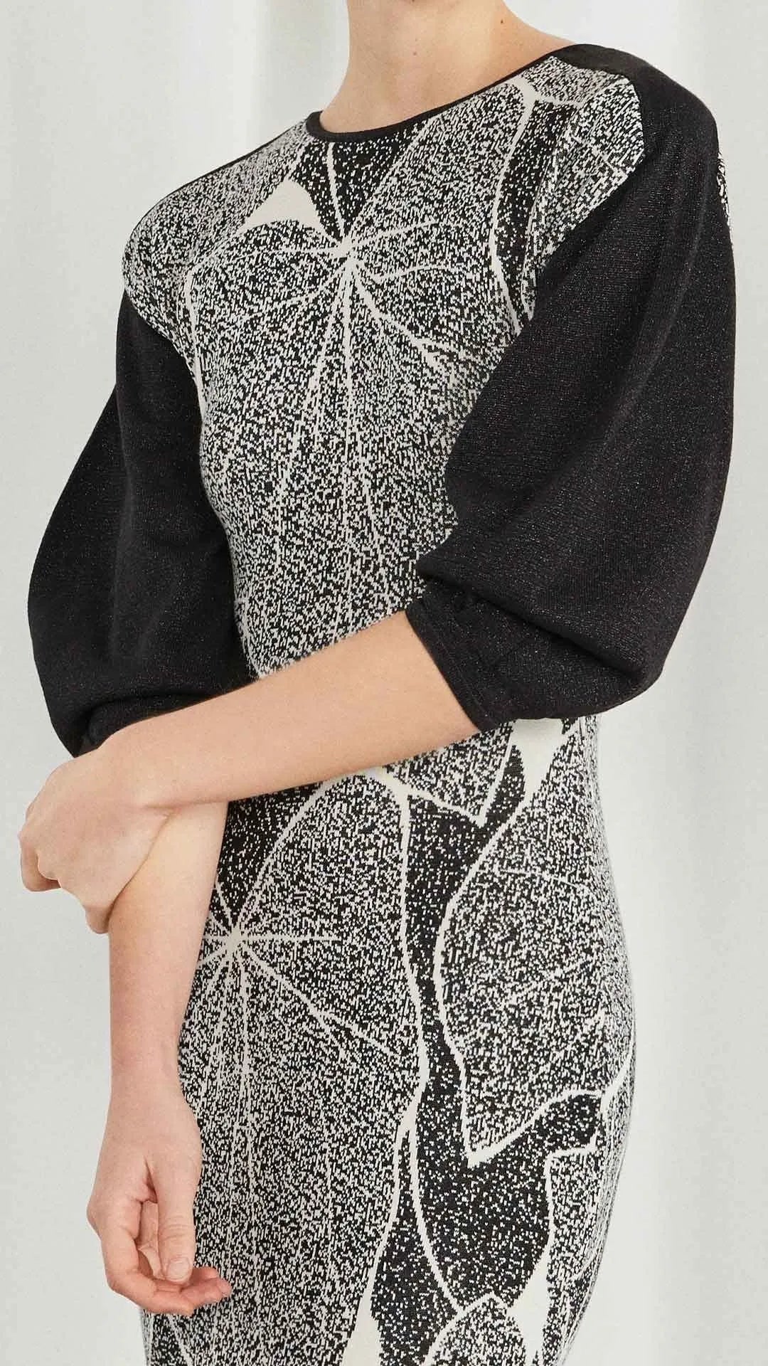 Clea Stuart Leaves Dress. Patterned in ecru and black silk knit with a hint of sparkle. It has contrasting black puffed sleeves and is full length. Shown in the model close up of the front.