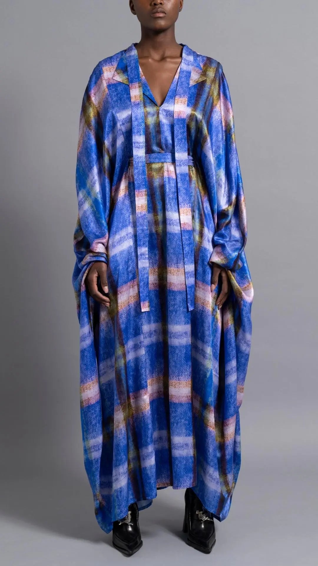 Thebe Magugu Blue Print Belted Kaftan. An elegant draped kaftan dress in blue with soft pink and grey striping. It features a V neck and can be belted to find the perfect fit for your body. It has long sleeves and is floor length. This photo shows the piece on the model facing front.