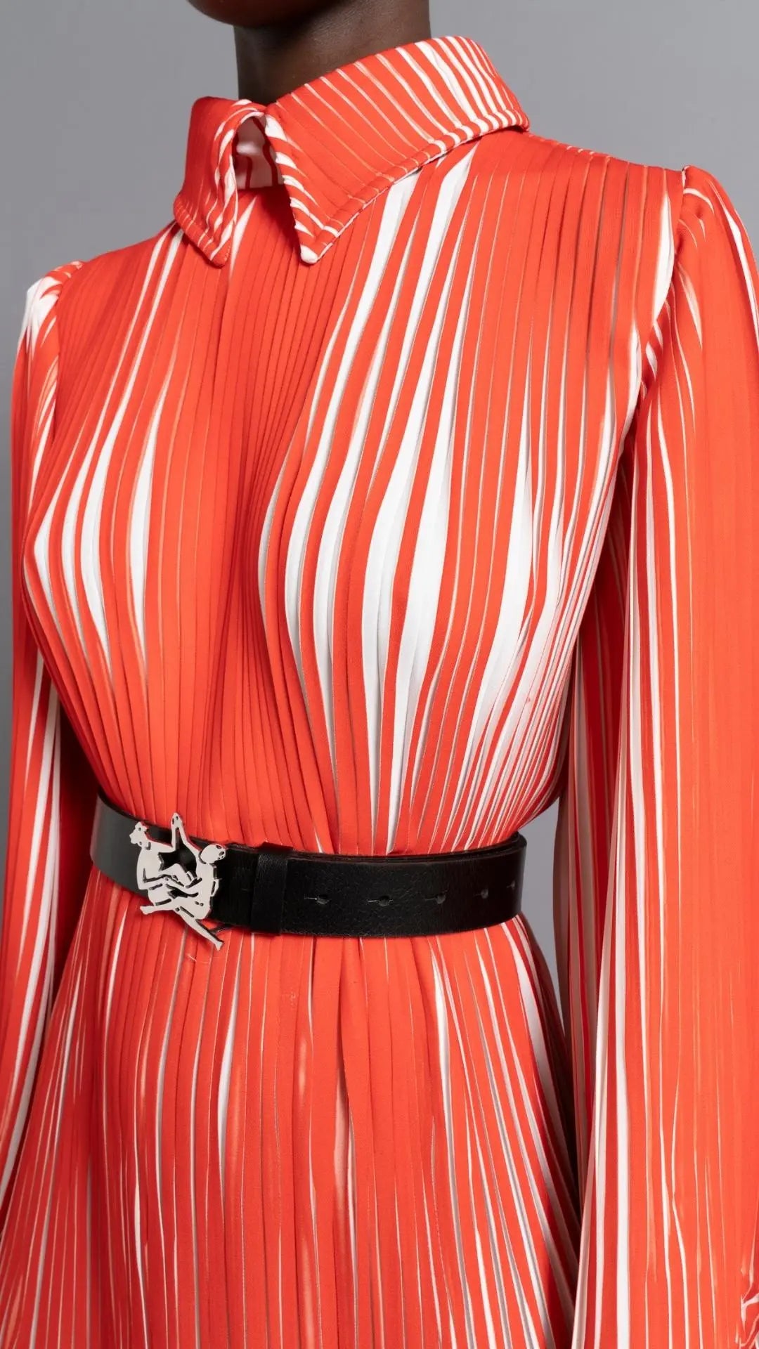 Thebe Magugu Chevron Pleated Dress. Stunning tomato red and white pleated dress with a collar, fitted waist and double chevron hem at the sleeves. It features a hidden zipper in the back. Close up of detailed pleated and collar.