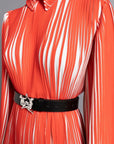 Thebe Magugu Chevron Pleated Dress. Stunning tomato red and white pleated dress with a collar, fitted waist and double chevron hem at the sleeves. It features a hidden zipper in the back. Close up of detailed pleated and collar.