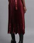 Thebe Magugu Chevron Pleated Skirt in a rich burgundy color. Fitted at the waist with straight pleats it falls into a double chevron pleat bottom. Long in length. It comes with a tie belt. Shown on model facing back with tie belt..