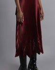 Thebe Magugu Chevron Pleated Skirt in a rich burgundy color. Fitted at the waist with straight pleats it falls into a double chevron pleat bottom. Long in length. It comes with a tie belt. Shown on model facing to the side.