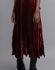 Thebe Magugu Chevron Pleated Skirt in a rich burgundy color. Fitted at the waist with straight pleats it falls into a double chevron pleat bottom. Long in length. It comes with a tie belt. Shown on model facing to the sise.
