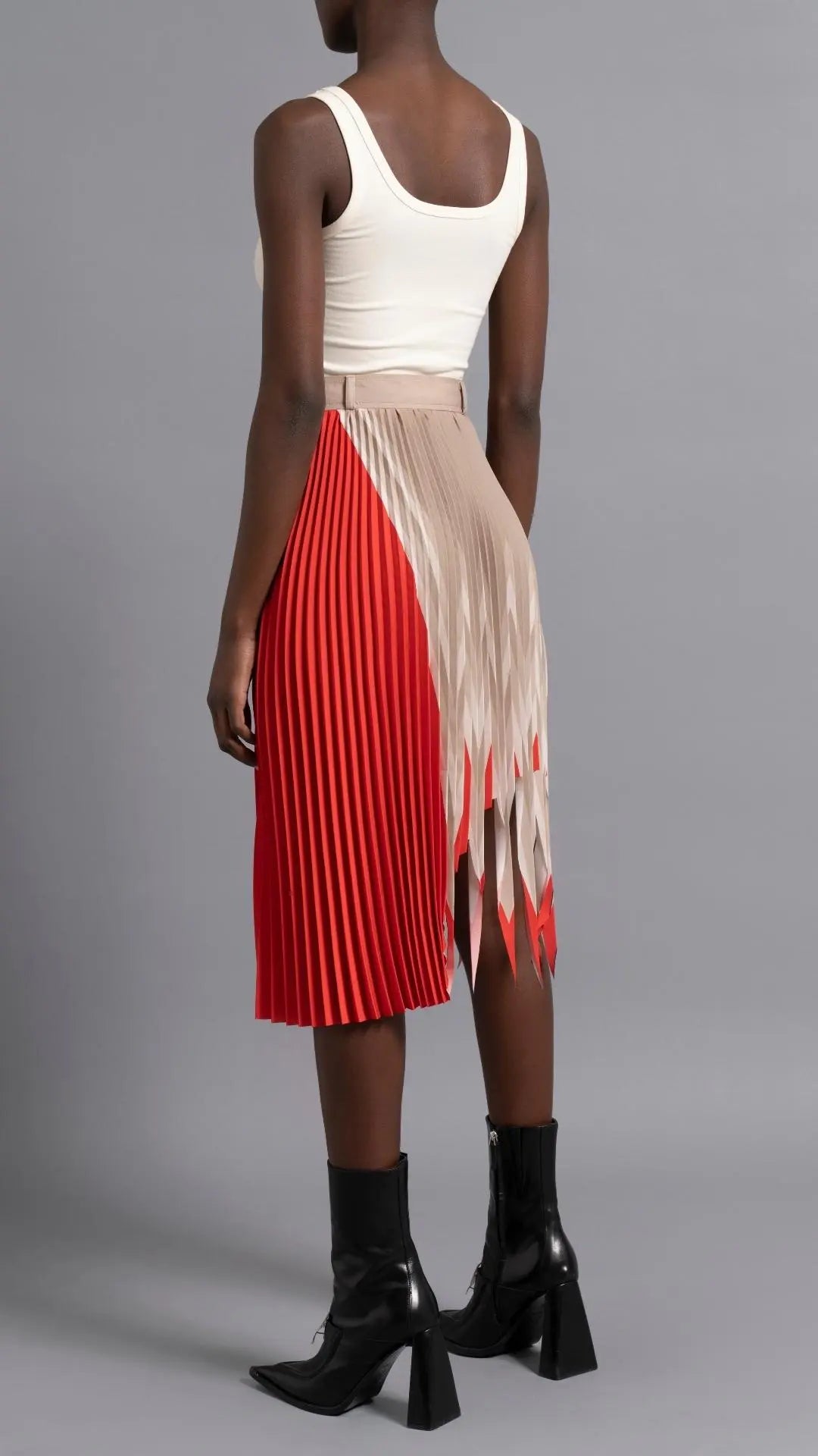 Thebe Magugu Shredded Pleated Skirt. Signature Thebe Magugu pleated skirt but with an asymmetrical twist in ecru, white and red. Shown on model facing back.