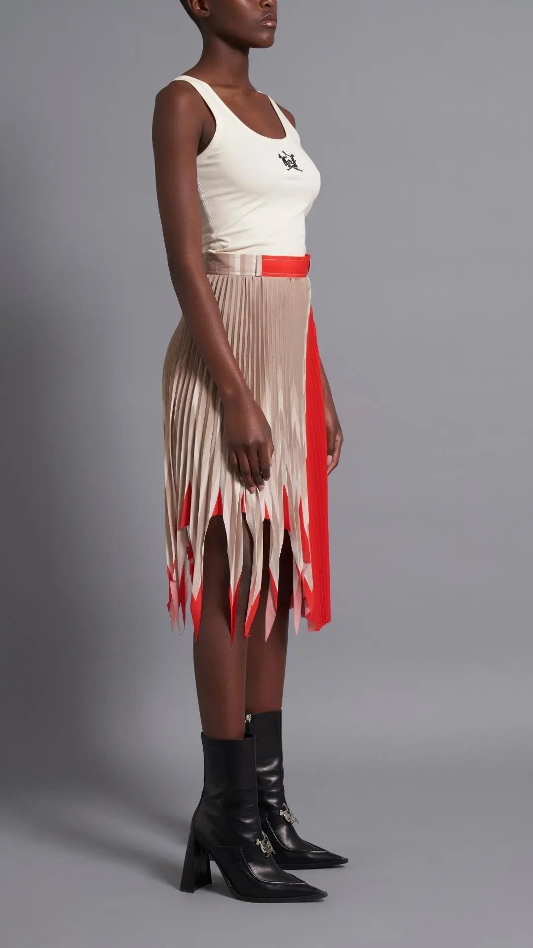 Thebe Magugu Shredded Pleated Skirt. Signature Thebe Magugu pleated skirt but with an asymmetrical twist in ecru, white and red. Shown on model facing side.